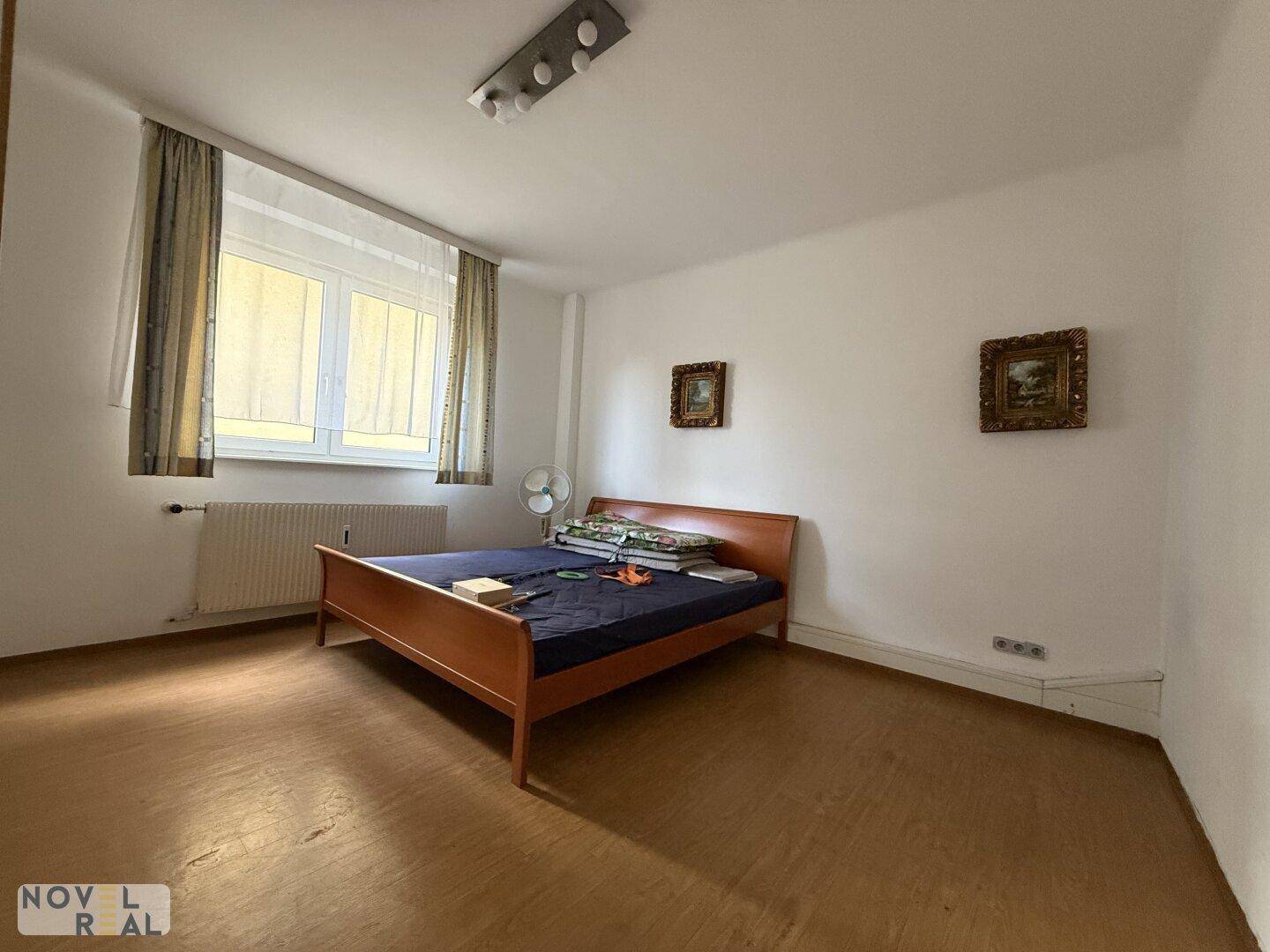 Schlafzimmer mit Holzboden, einem Doppelbett und einem Fenster mit Vorhängen für Privatsphäre.