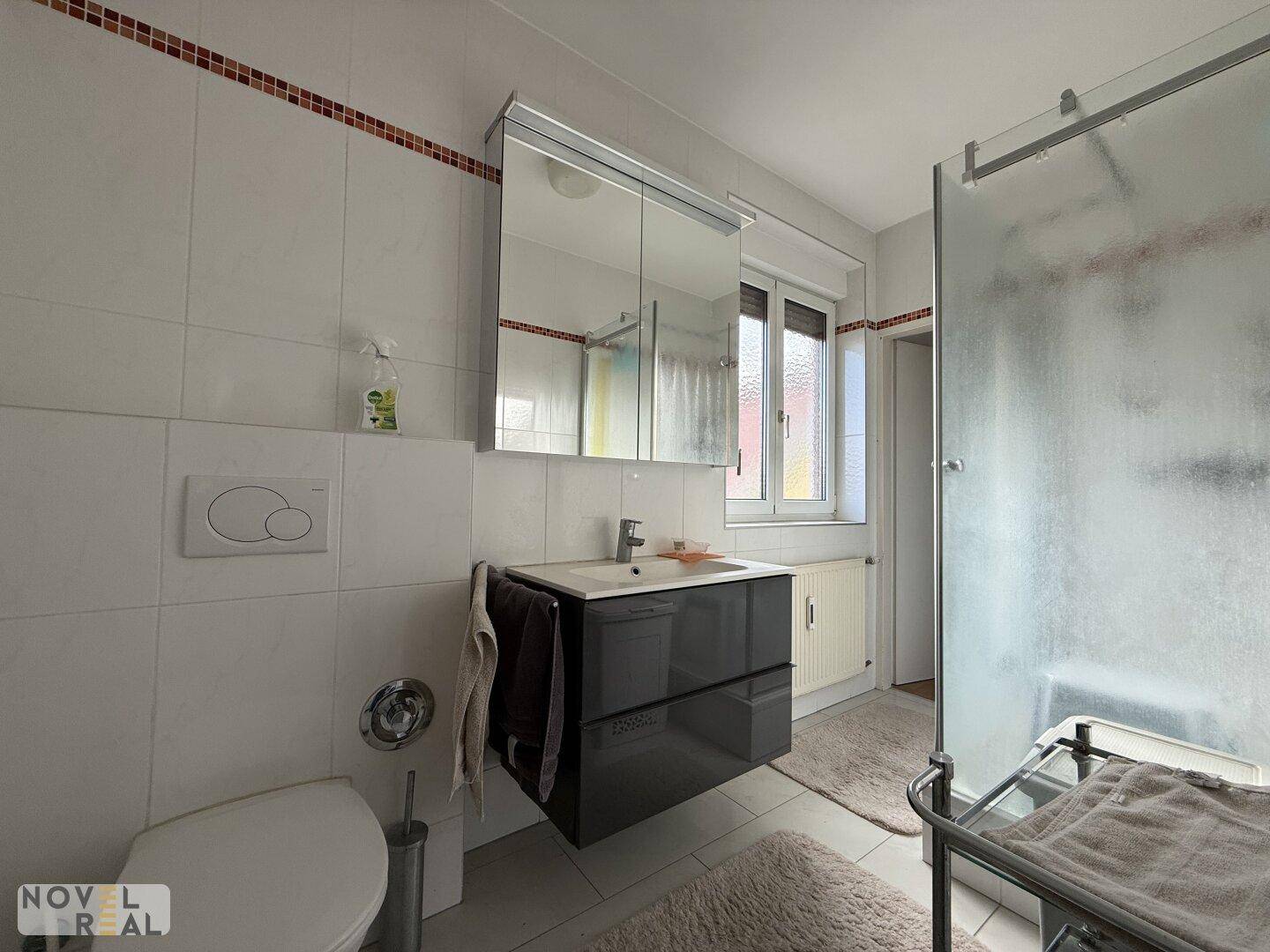 Modernisiertes Badezimmer mit Hängeschrank, Waschbeckenunterschrank und Duschkabine.