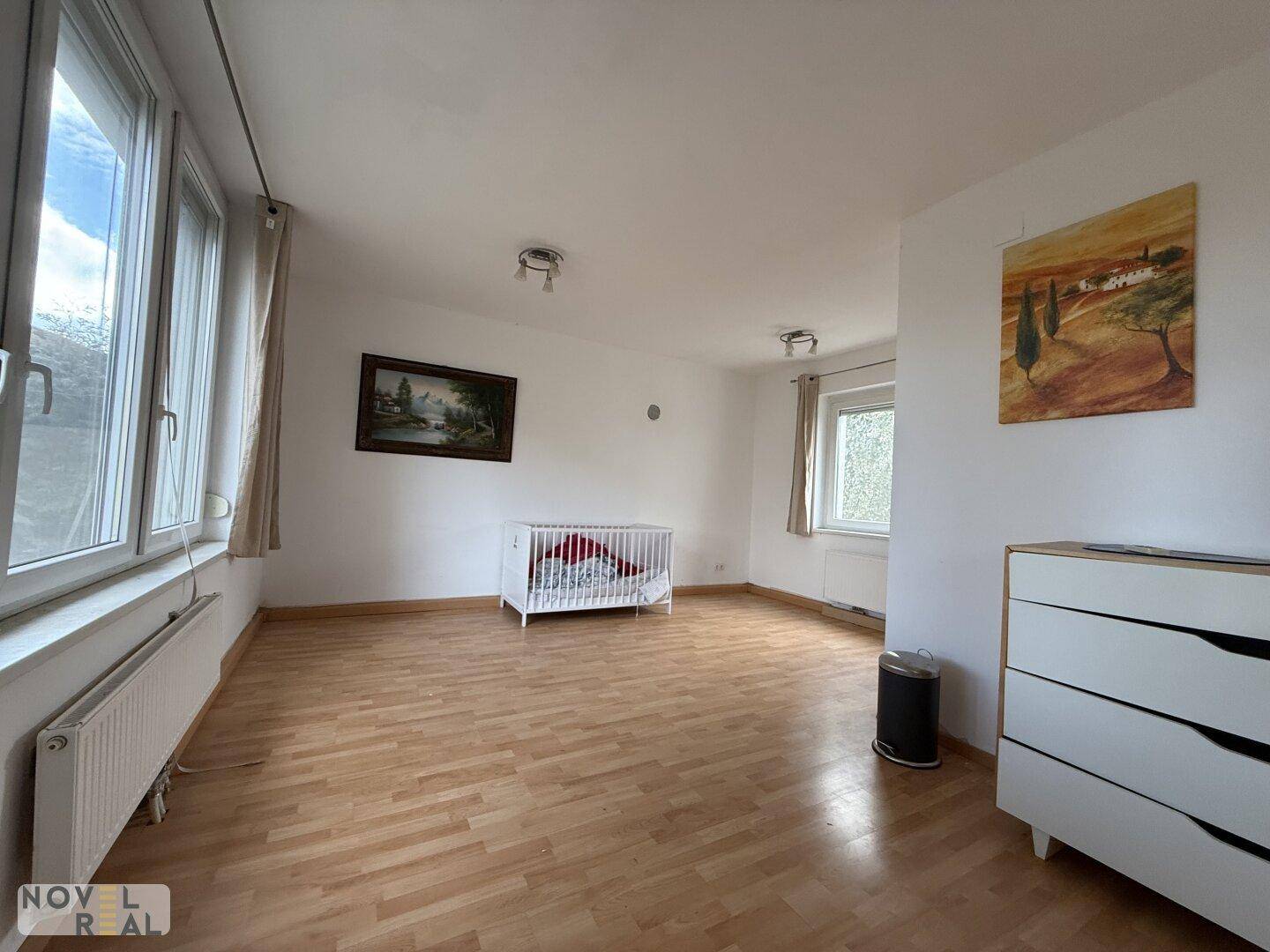 Helles und geräumiges Zimmer mit Holzboden und großen Fenstern, ideal als Kinderzimmer.