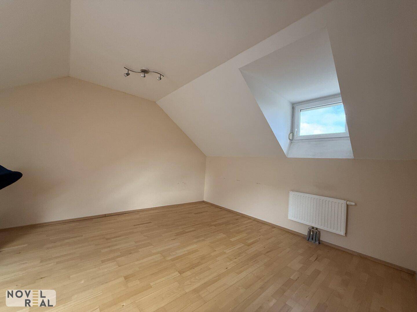 Leeres Dachgeschosszimmer mit Holzboden, Dachschräge und einem hellen Dachfenster.