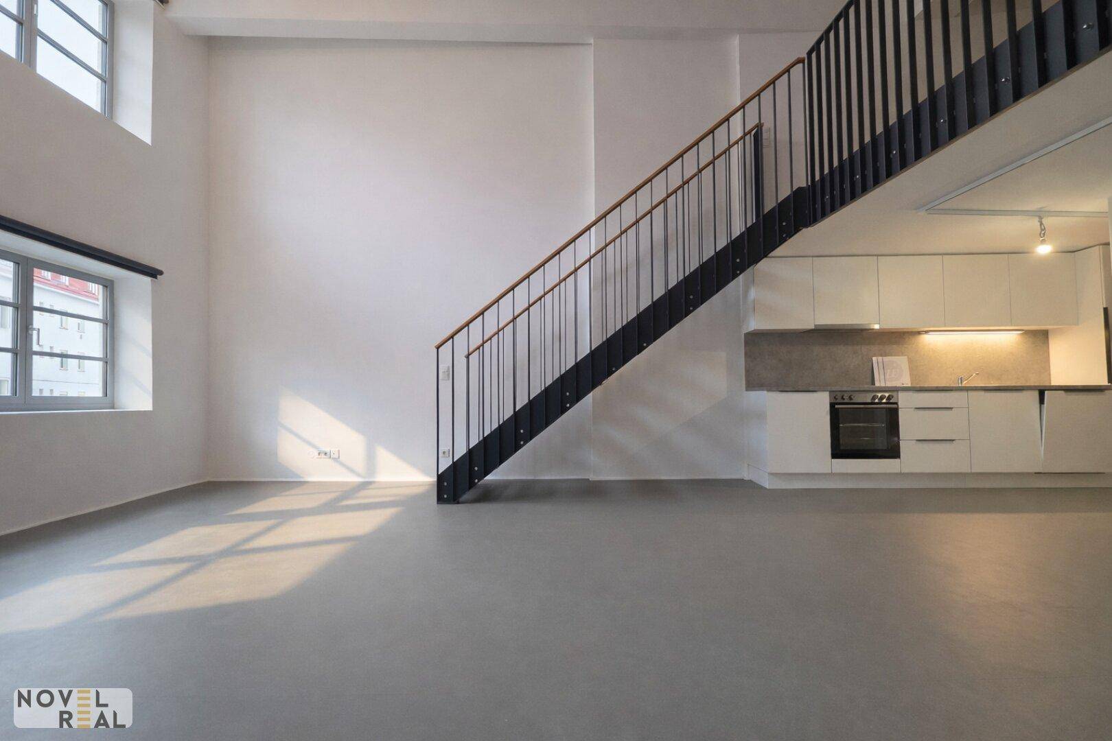 Lichtdurchfluteter Wohnbereich mit minimalistischer Küche und Treppe in einem modernen Loft.