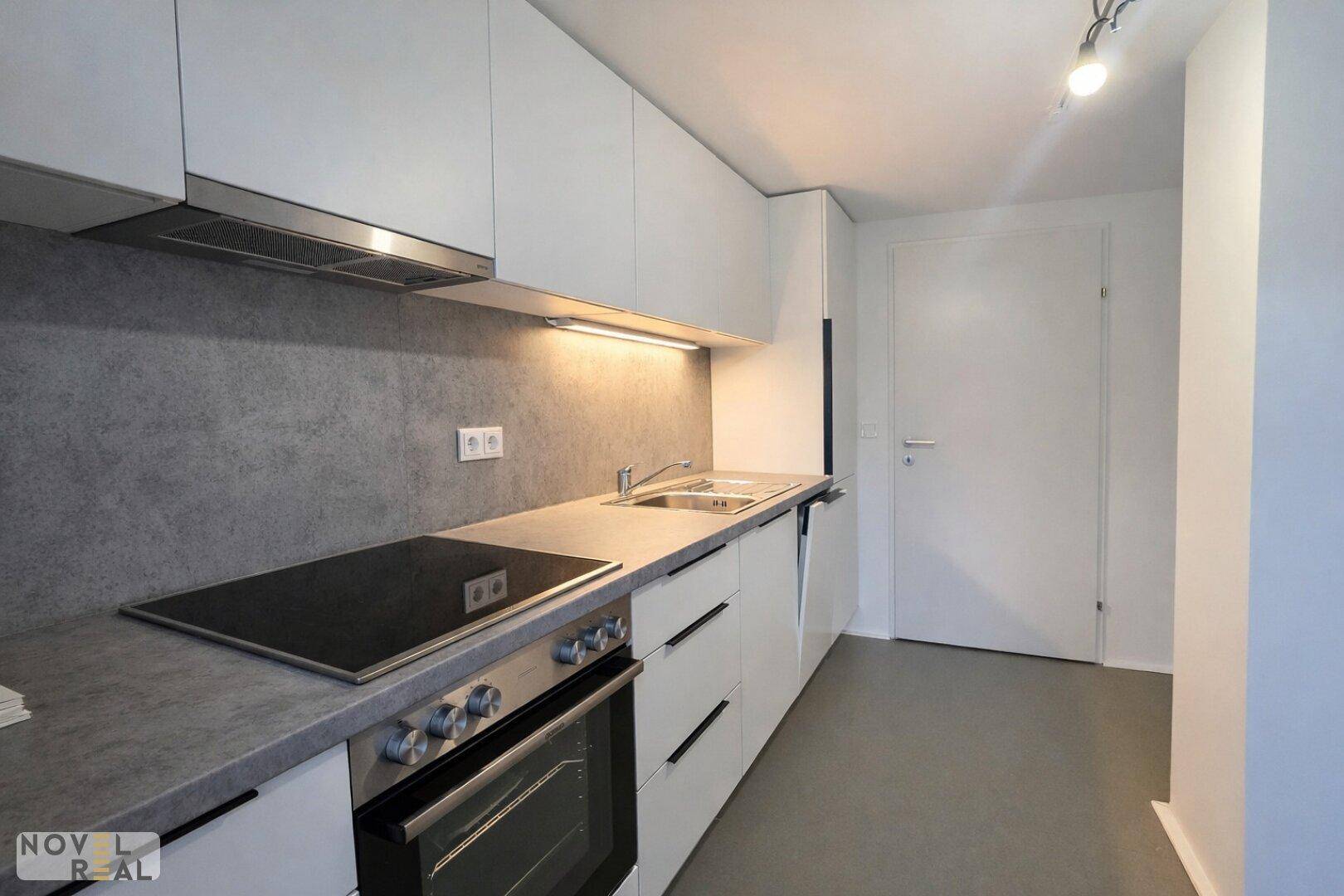 Moderne Einbauküche mit grauer Arbeitsplatte, Induktionskochfeld und integriertem Backofen.