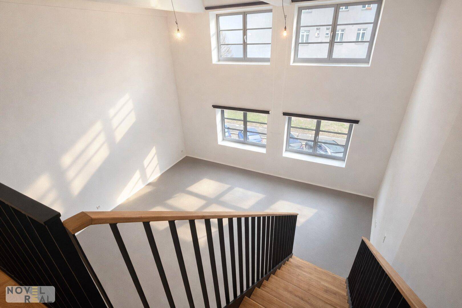 Blick von der Treppe auf den hellen Wohnbereich mit hohen Fenstern und viel Tageslicht.