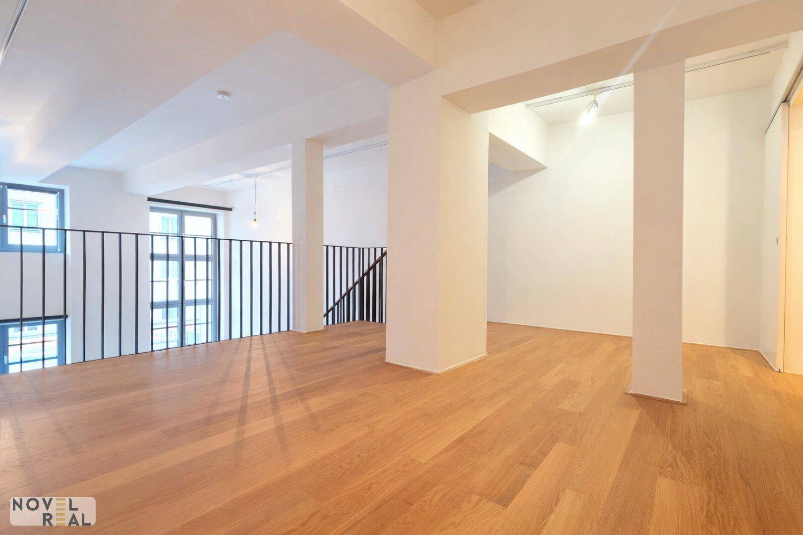 Obere Galerie mit Holzboden und Blick auf den unteren Wohnbereich durch die Fenster.