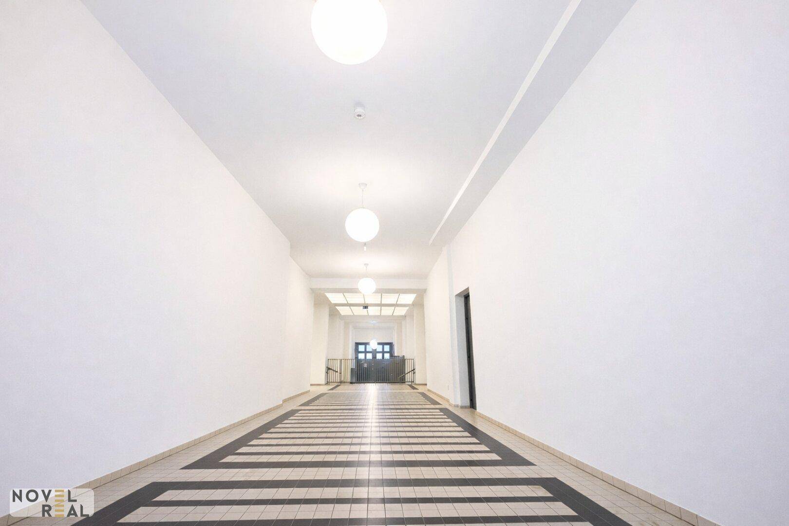 Langer, heller Flur mit markantem Bodenmuster und modernen Deckenleuchten.