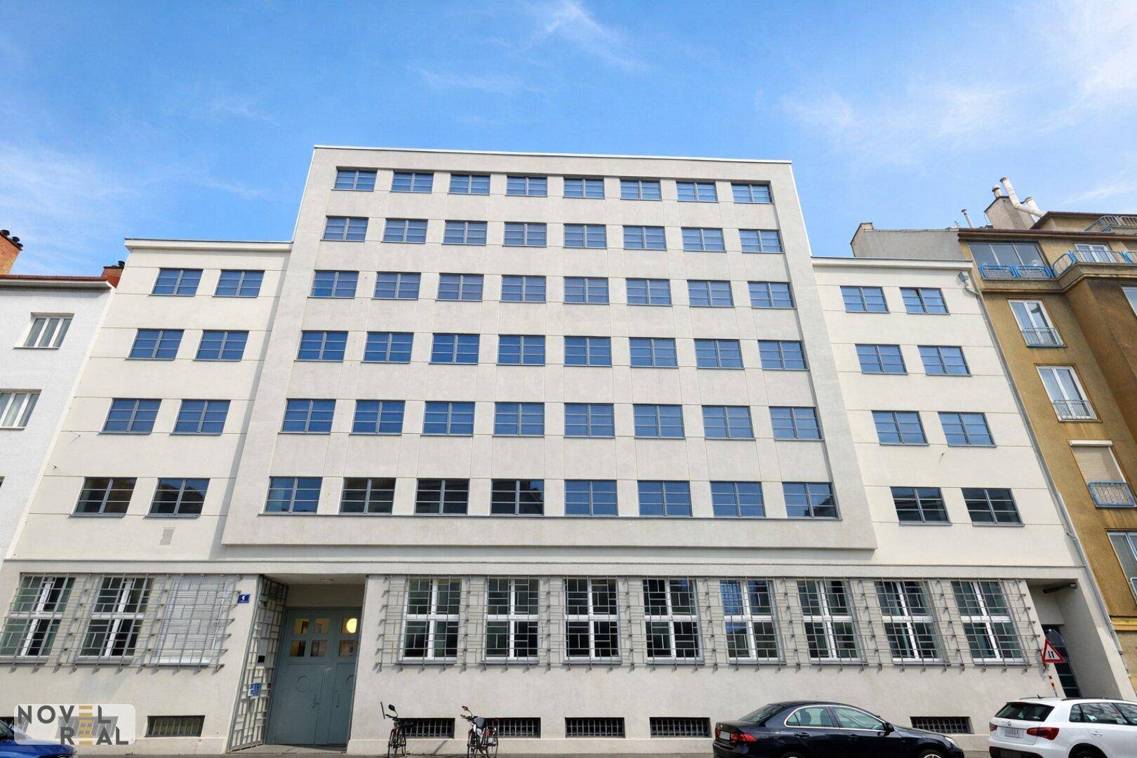 Moderne Gebäudefassade mit vielen Fenstern und klaren Linien unter blauem Himmel.