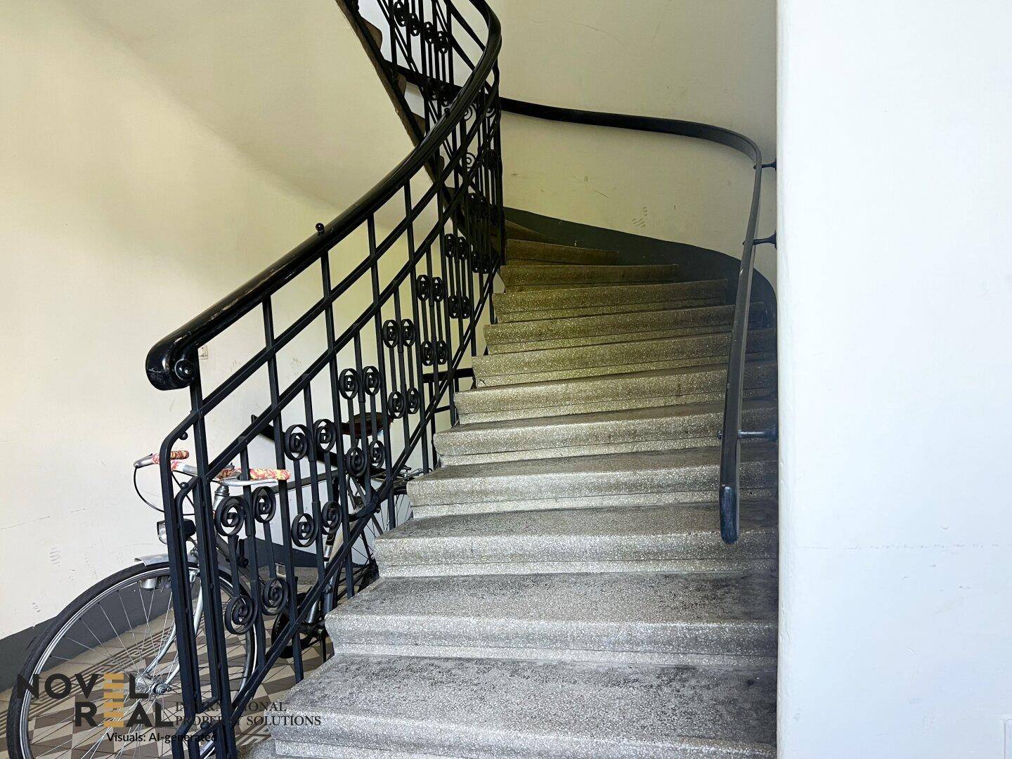 Geschwungenes Treppenhaus mit schmiedeeisernem Geländer und Steinstufen.