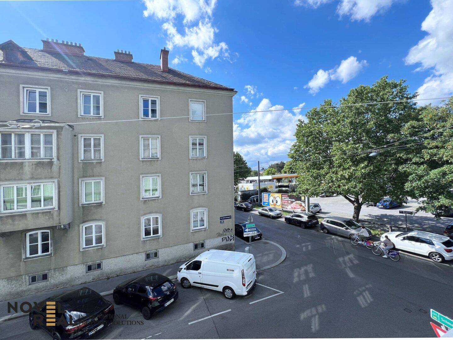 Blick von oben auf eine belebte Straße mit parkenden Autos und Bäumen.
