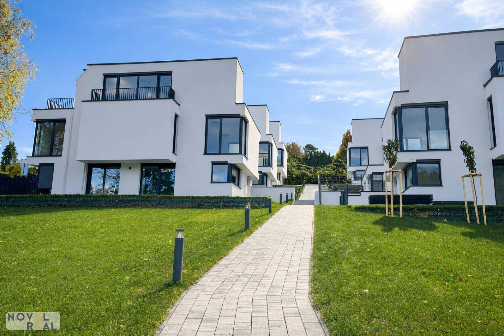 Mehrere moderne weiße Gebäude mit großen Fenstern und gepflegten Rasenflächen unter strahlendem Sonnenschein.