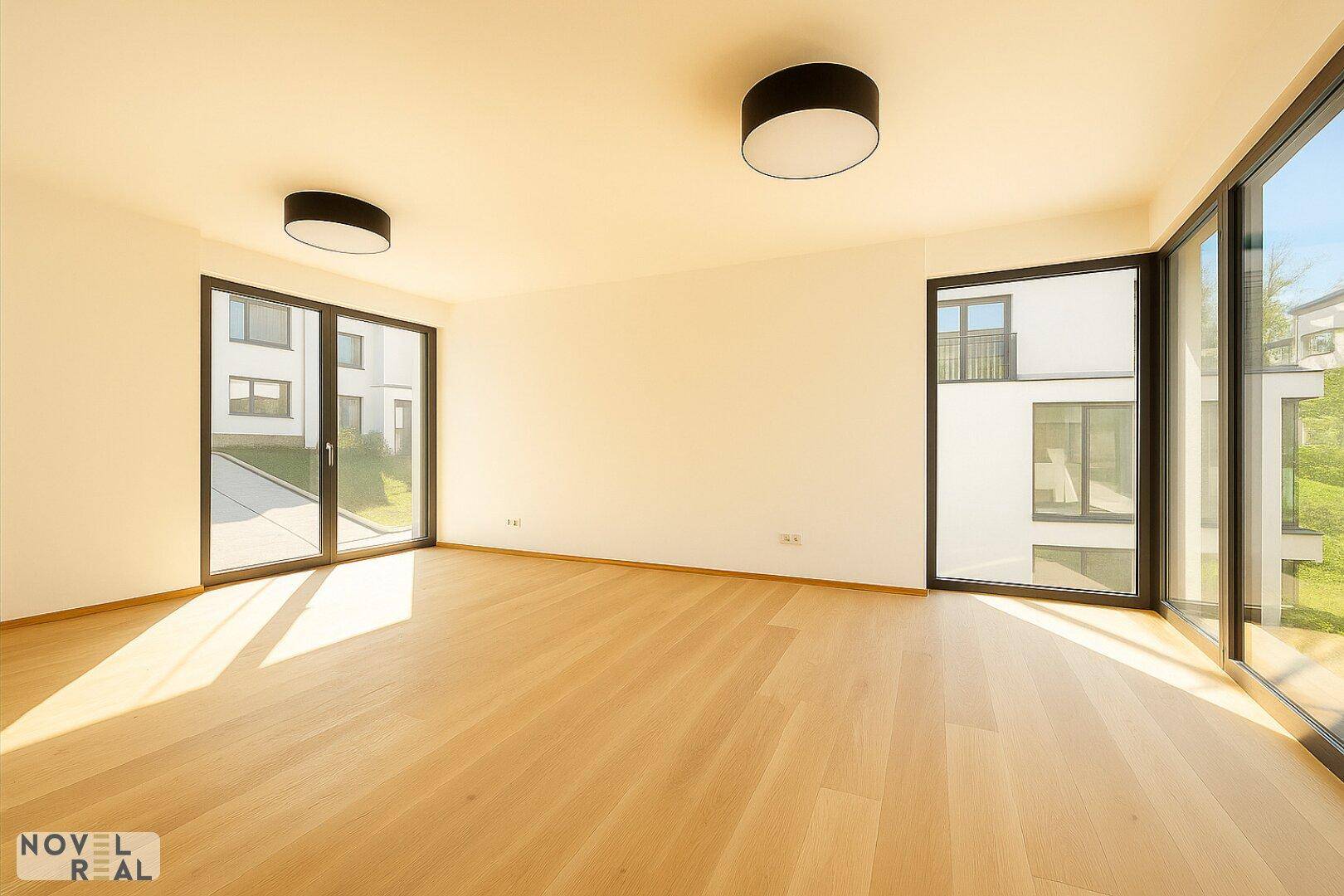 Heller Wohnraum mit großen Fenstern, die viel Sonnenlicht hereinlassen, und modernem Holzboden.