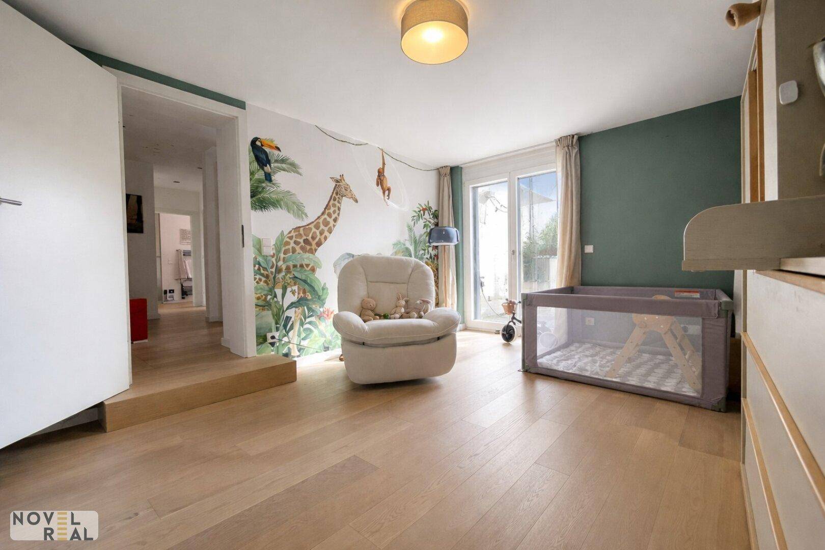 Freundliches Kinderzimmer mit verspielter Wanddekoration, Holzboden und viel Tageslicht.