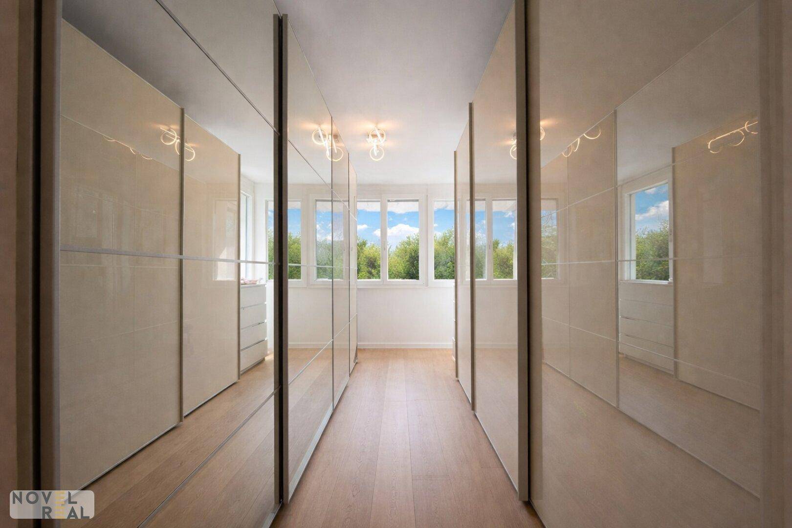 Geräumiger begehbarer Kleiderschrank mit Spiegeltüren und viel Tageslicht.