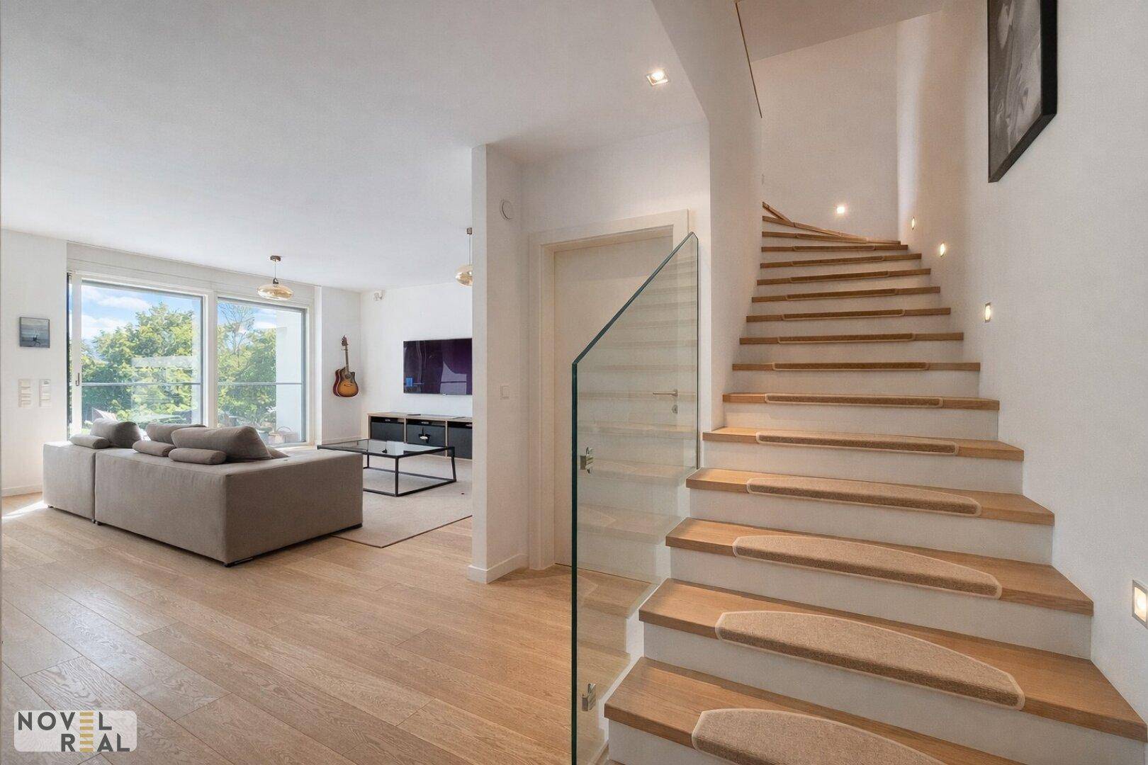 Heller Eingangsbereich mit moderner Holztreppe und Blick in das offene Wohnzimmer.