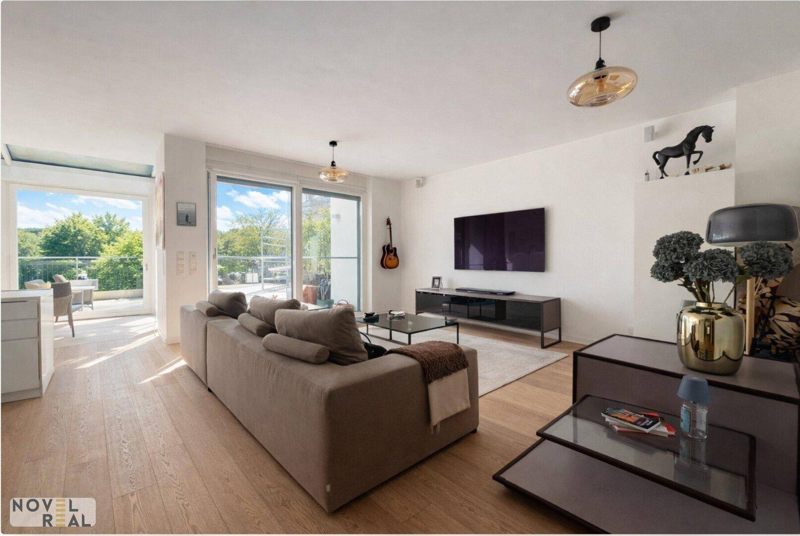 Modernes Wohnzimmer mit Holzboden, großem Sofa und Zugang zum Balkon mit Grünblick.