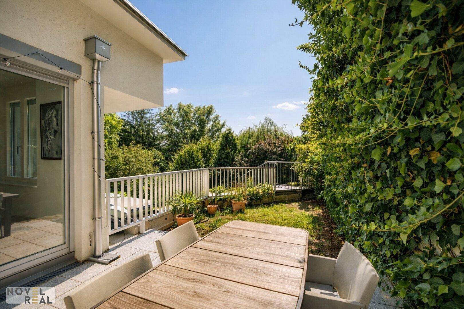Balkon mit Esstisch und Stühlen, umgeben von üppigem Grün und mit weitem Blick.
