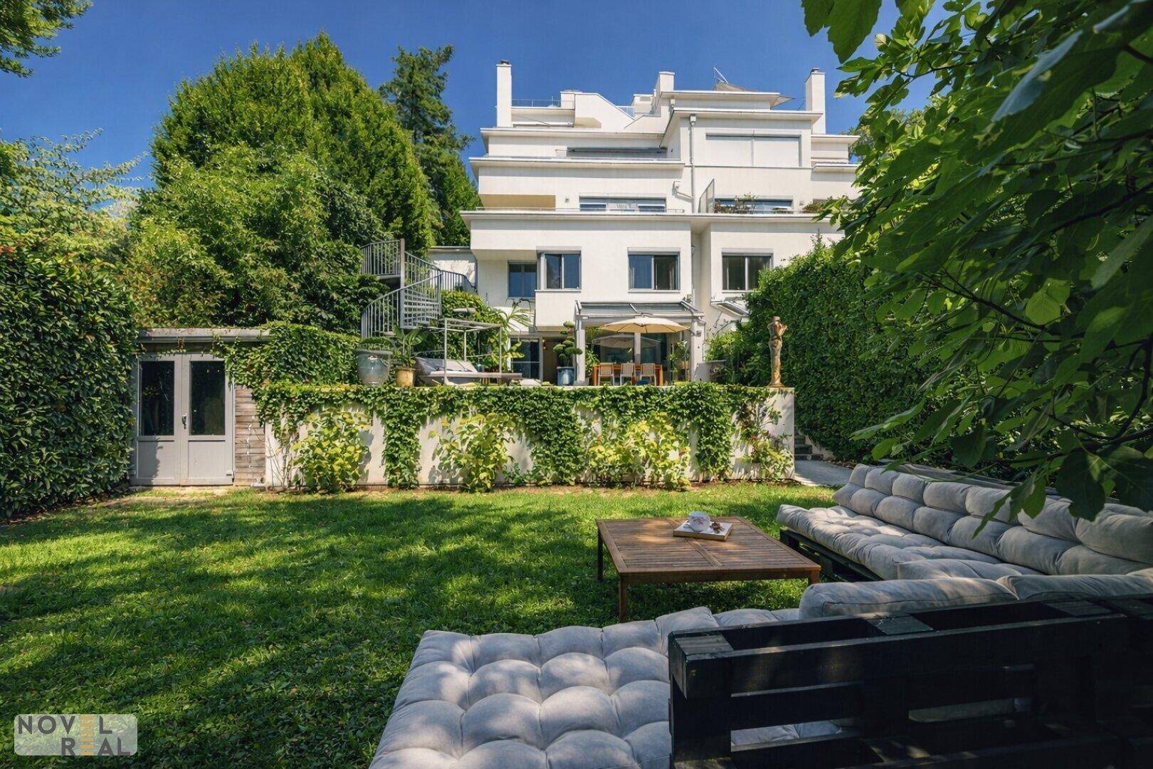 Großer Rasengarten mit bequemer Lounge-Sitzgruppe und Blick auf die moderne Villa.