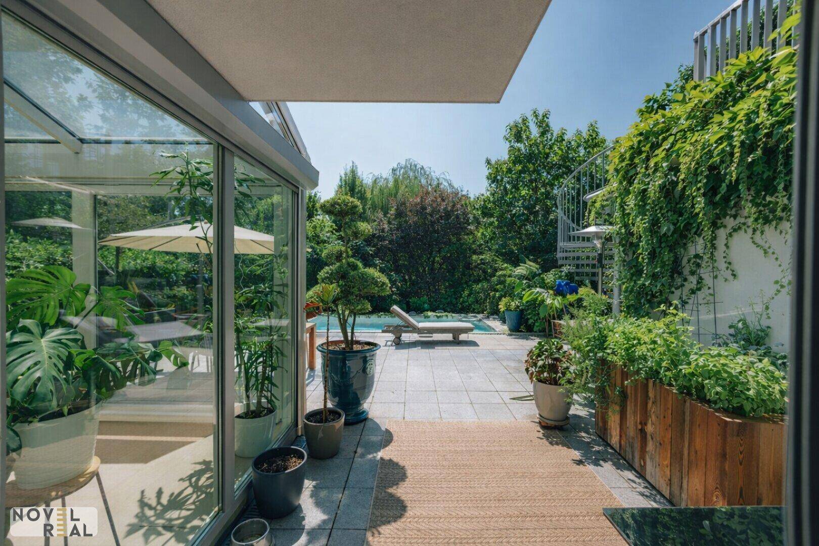 Gepflasterte Terrasse mit vielen Pflanzen und Blick auf den Poolbereich im Garten.