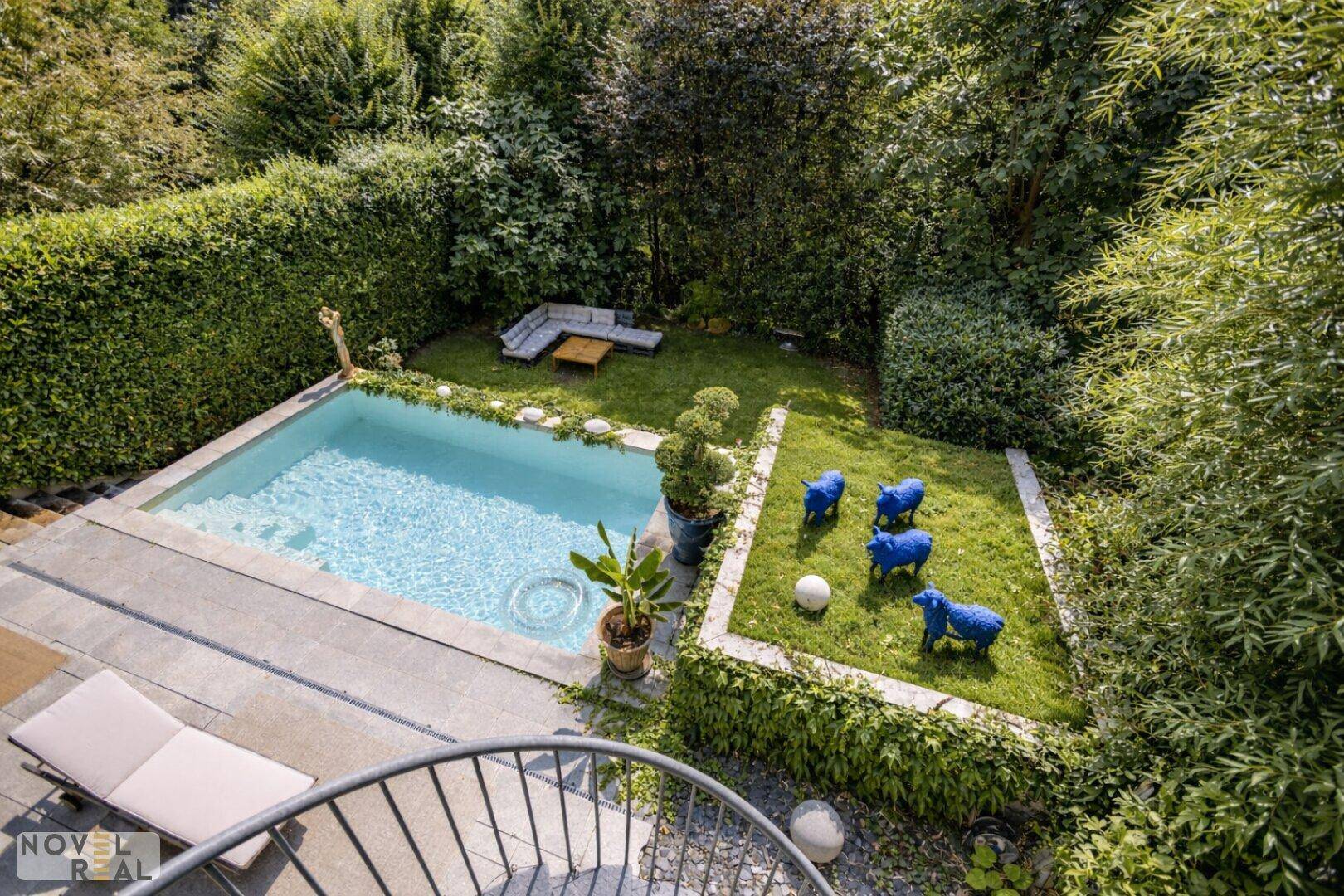 Vogelperspektive auf den Garten mit kleinem Pool, Liegewiese und blauen Dekorationen.