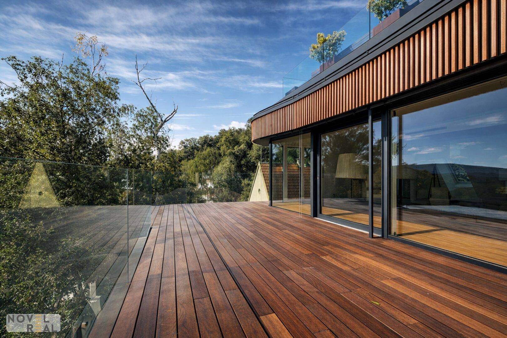 Große Holzterrasse mit raumhohen Fenstern und Glasgeländer, umgeben von Bäumen und Natur.