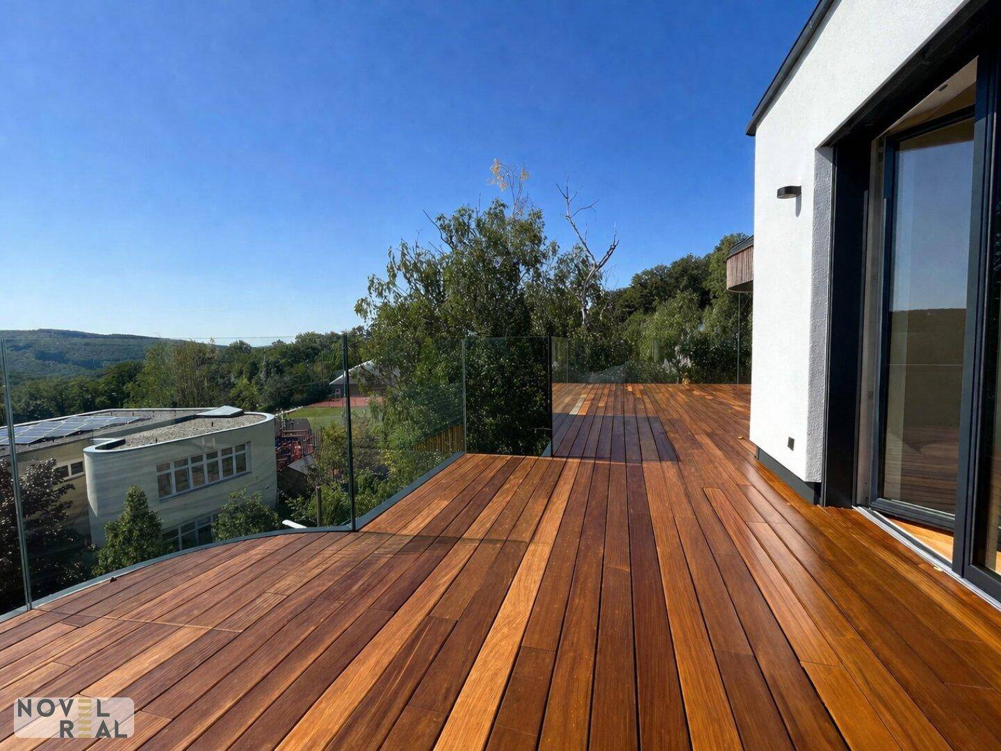 Geräumige Holzterrasse mit elegantem Glasgeländer und weitem Blick in die grüne Umgebung.