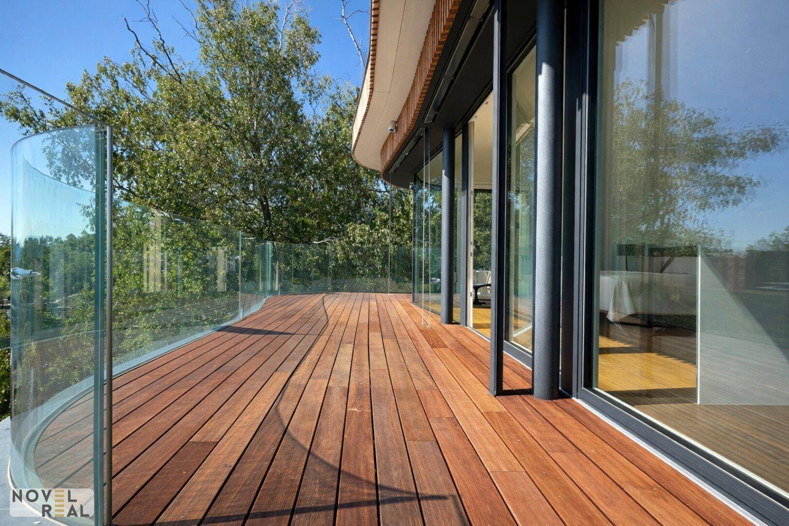 Geschwungene Holzterrasse mit Glasgeländer und Panoramablick auf die umliegende Natur und Landschaft.
