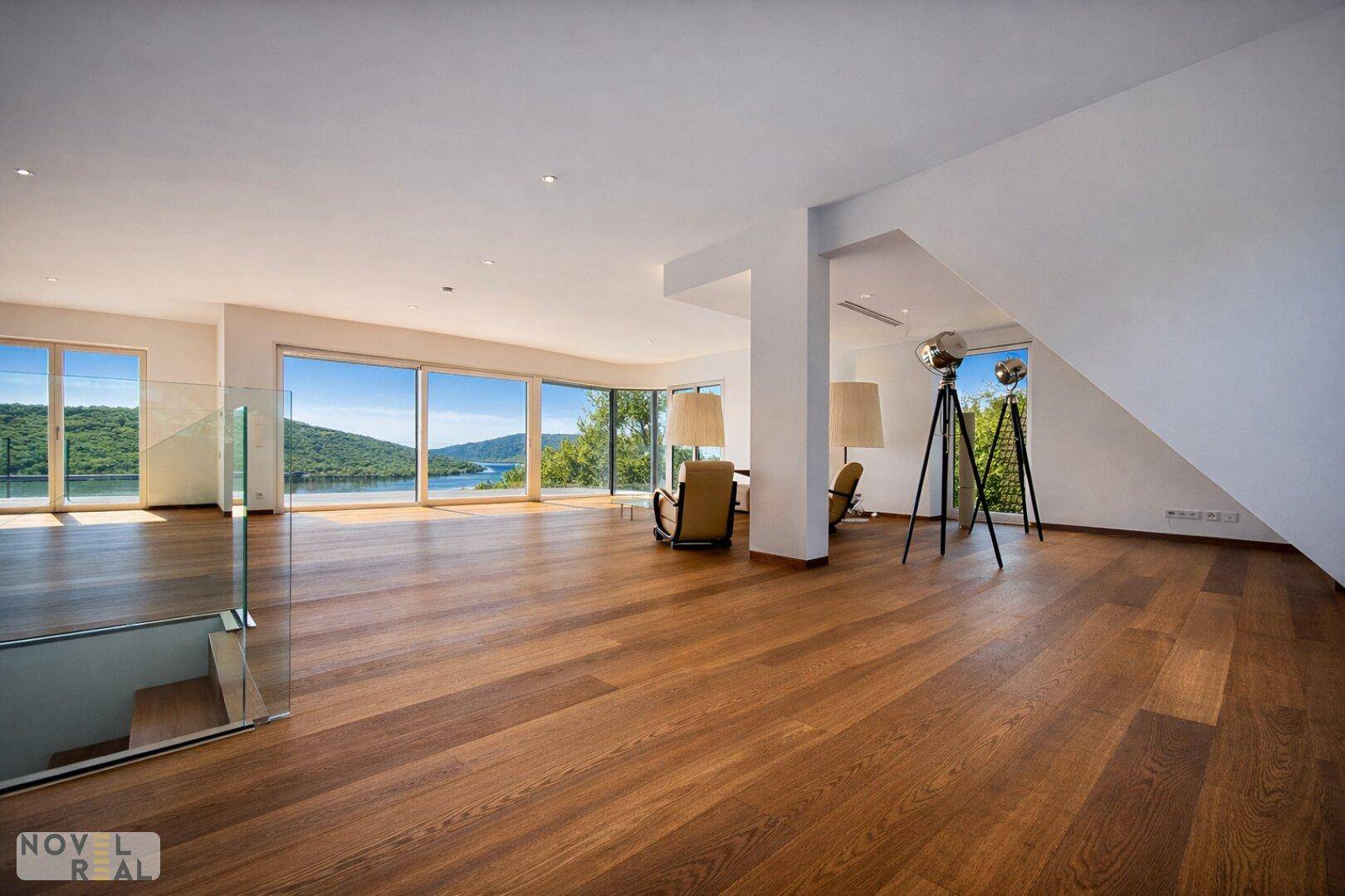 Großzügiges Wohnzimmer mit Holzboden, raumhohen Fenstern und Panoramablick auf den See und die Natur.