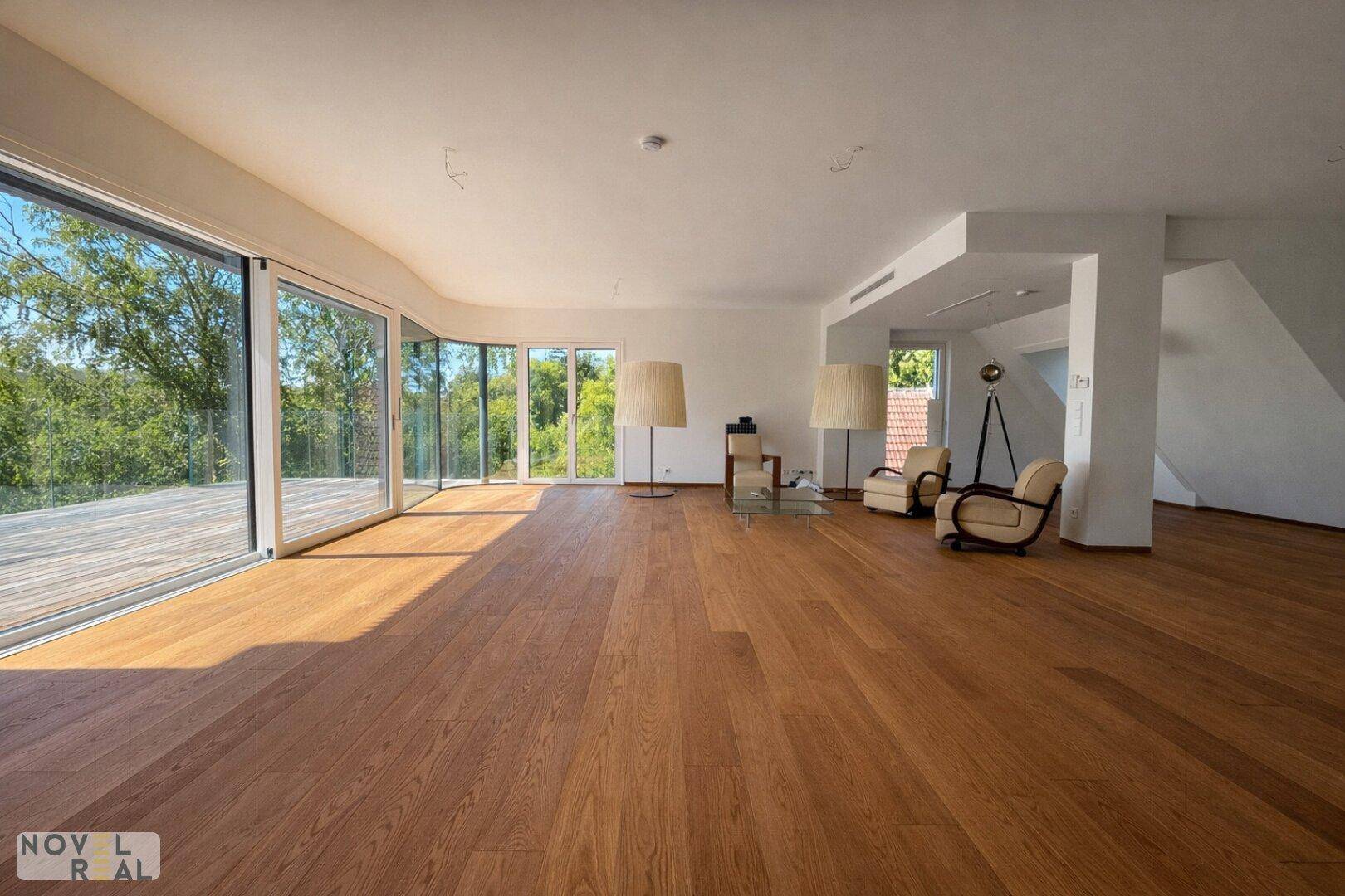 Geräumiges Wohnzimmer mit Holzboden, viel Tageslicht und weitem Blick ins Grüne.