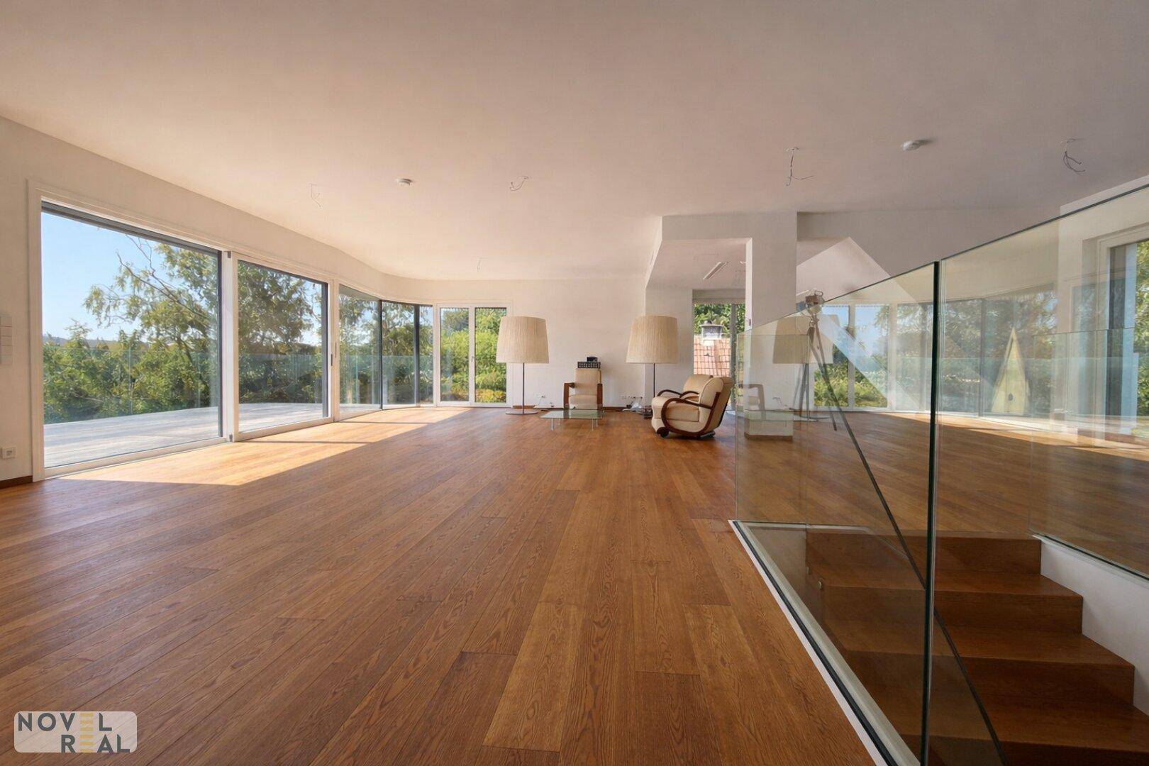 Helles Wohnzimmer mit Holzboden, großen Fenstern und direktem Zugang zu einer Außenterrasse.
