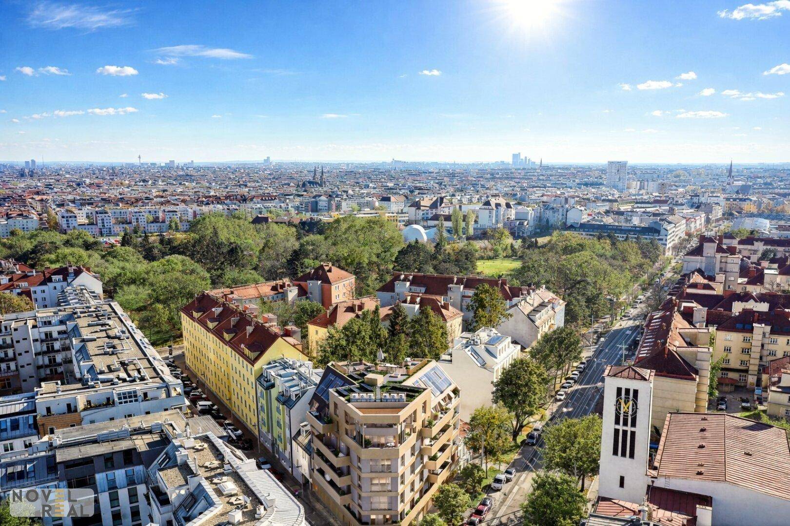 Weitläufige Luftaufnahme einer Stadt mit vielen Gebäuden, Grünflächen und einem Fluss im Hintergrund.