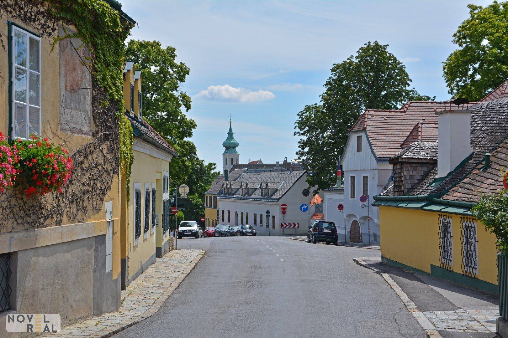Idyllische Gasse mit historischen Gebäuden und einem Kirchturm in der Ferne.