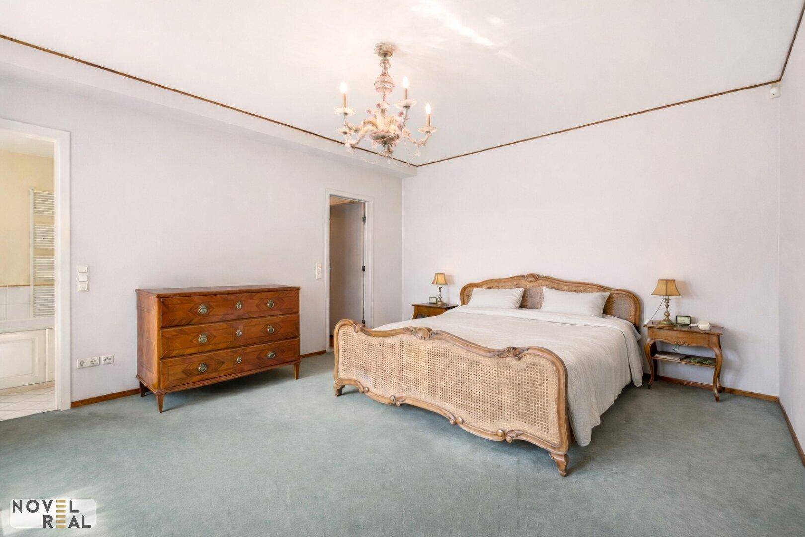 Helles Schlafzimmer mit Teppichboden, klassischem Bett und Kronleuchter.