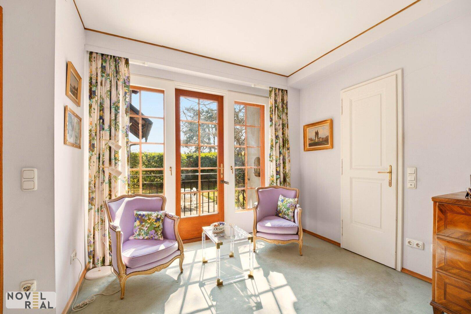 Helles Zimmer mit Teppichboden, floralen Vorhängen und Zugang zum französischen Balkon.