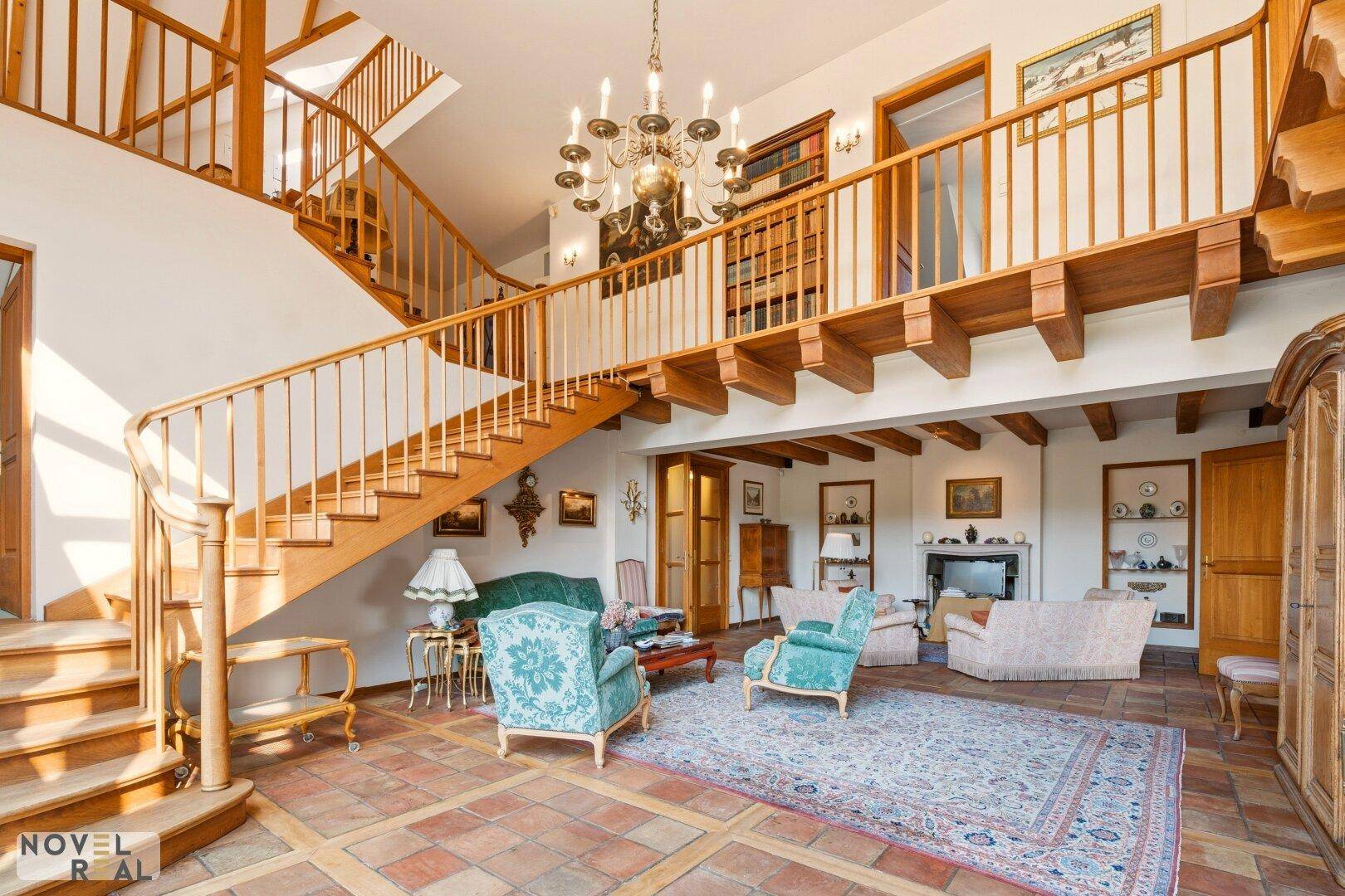 Geräumiger Wohnbereich mit Holzbalkendecke, eleganter Treppe und klassischem Mobiliar.