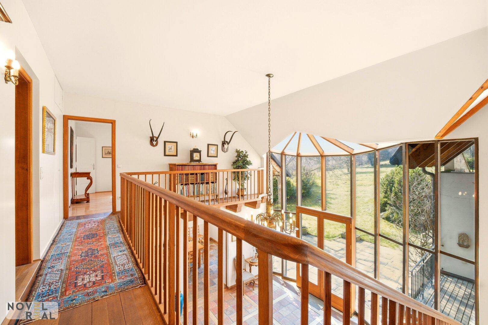 Geräumiger Flur im Obergeschoss mit Holzboden und Blick auf den Wintergarten und Garten.