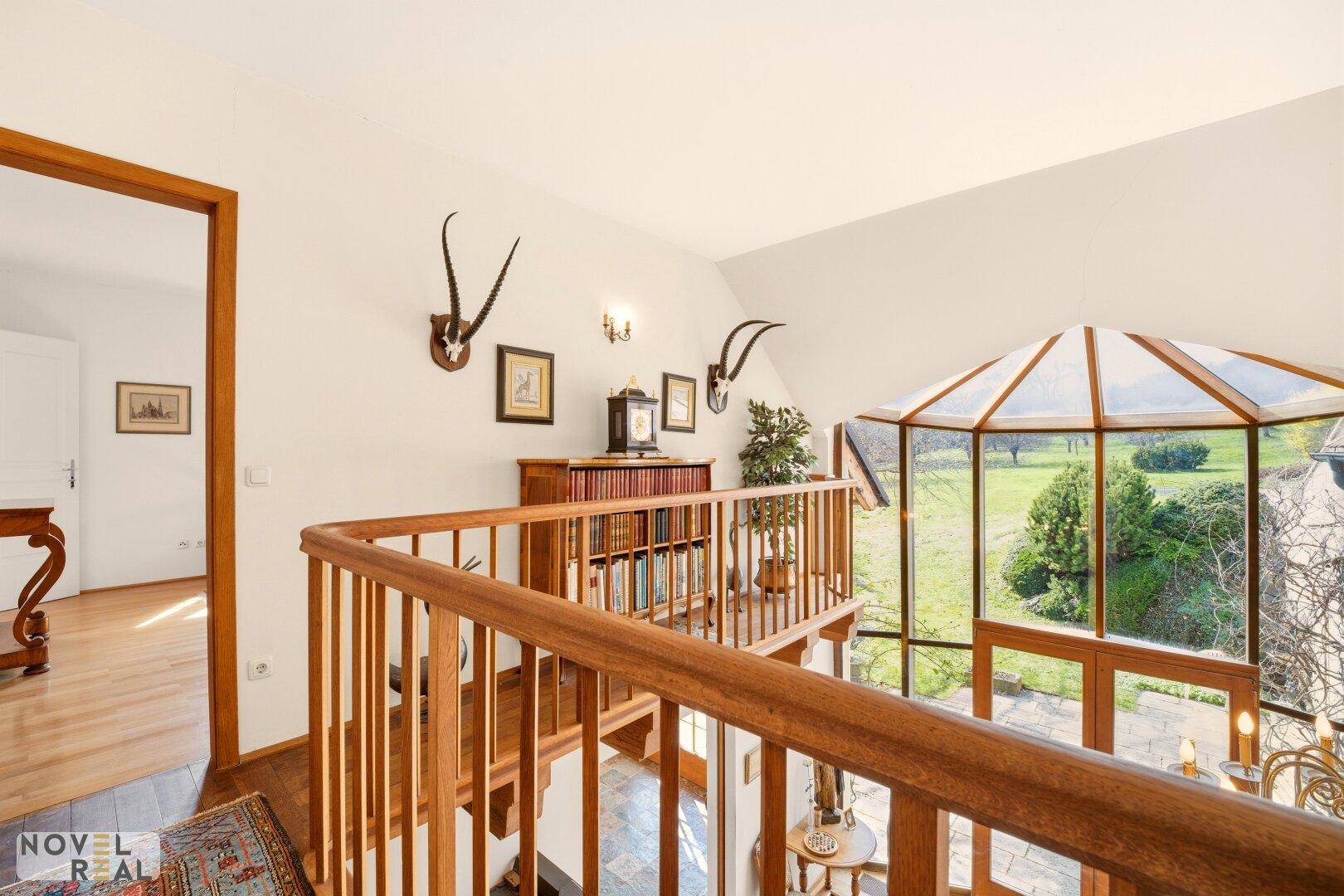 Heller Flur mit Holzboden, Bücherregal und Blick auf den Wintergarten und die Landschaft.