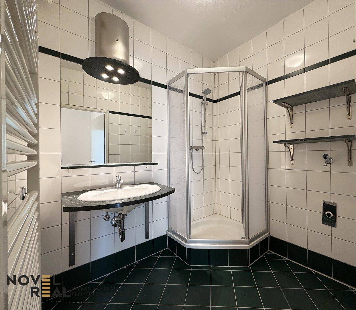 Badezimmer mit Duschkabine, Waschbecken und beheiztem Handtuchhalter, gefliest in Weiß und Schwarz.