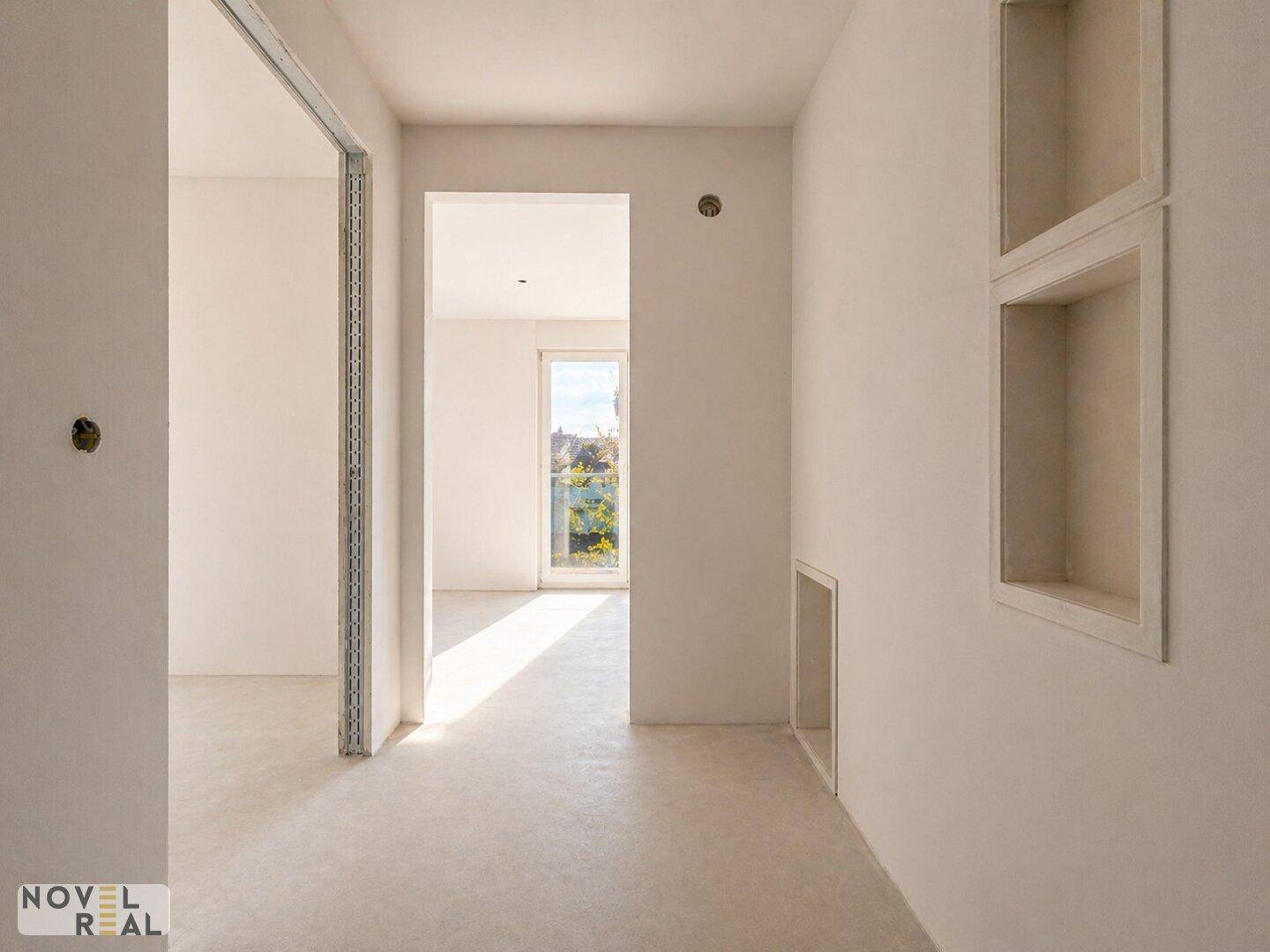 Heller Flur im Rohbau mit Nischen in der Wand und Zugang zu weiteren Räumen.