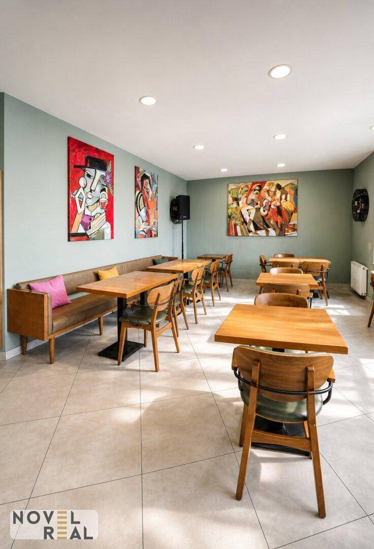 Heller Restaurantbereich mit modernen Holztischen, bequemen Sitzbänken und farbenfrohen Kunstwerken an den Wänden.