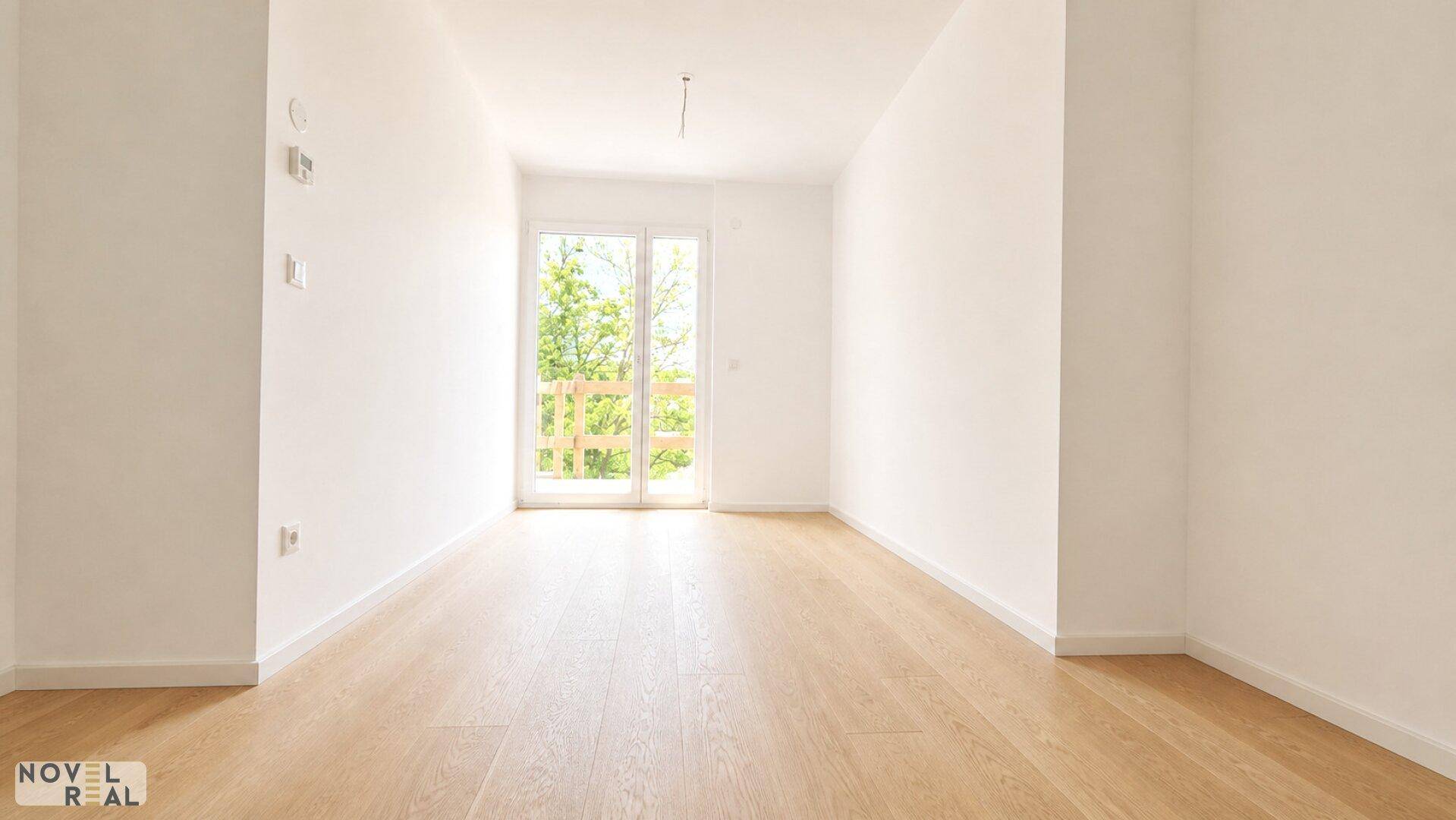Helles Zimmer mit Holzboden und Zugang zu einem französischen Balkon, bietet viel Tageslicht.