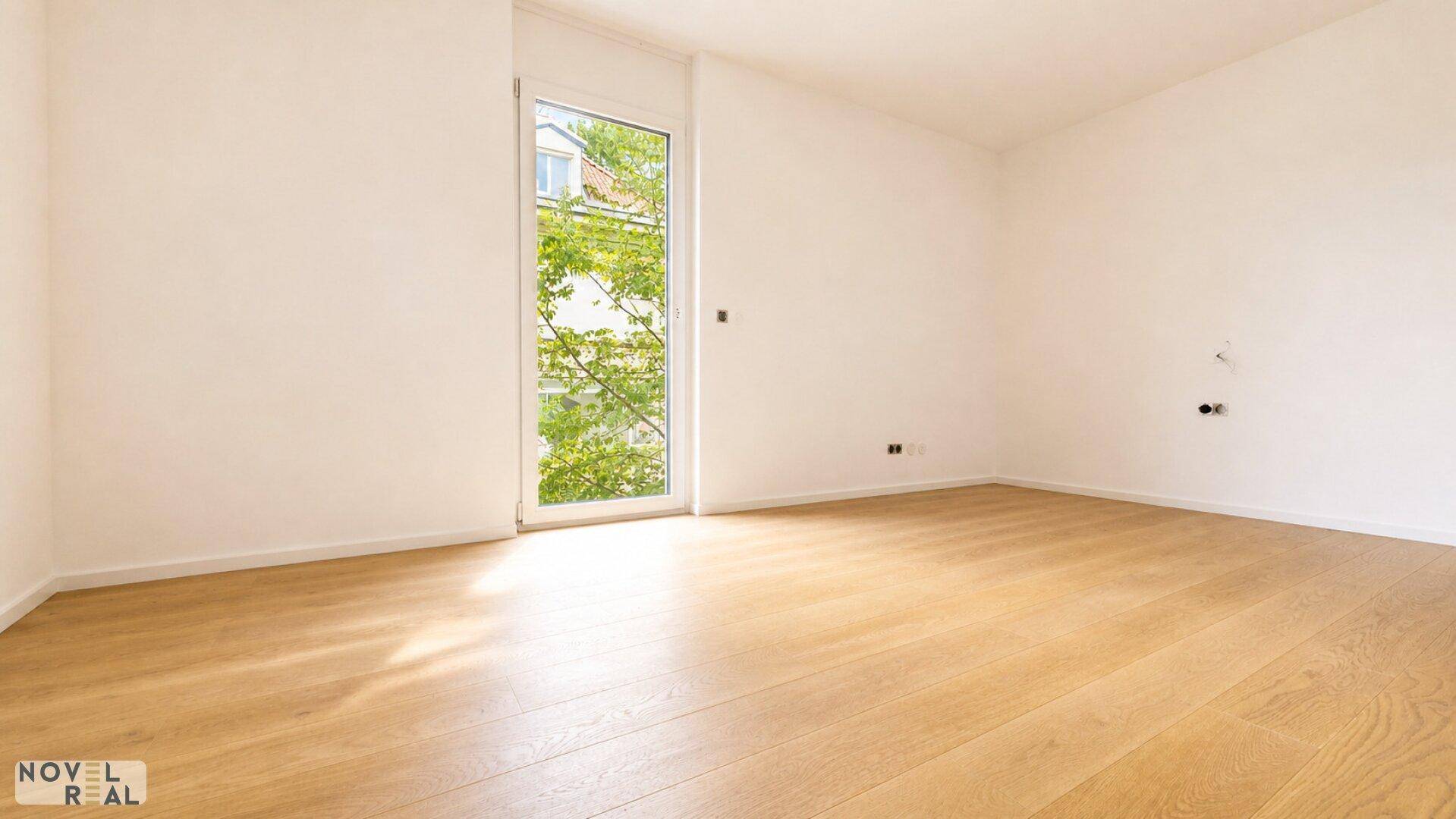 Helles Zimmer mit Holzboden und großem Fenster mit Blick auf die Umgebung.