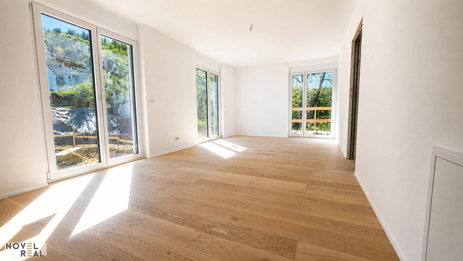 Lichtdurchflutetes Wohnzimmer mit hellem Holzboden und großen Fenstern mit Blick ins Grüne.
