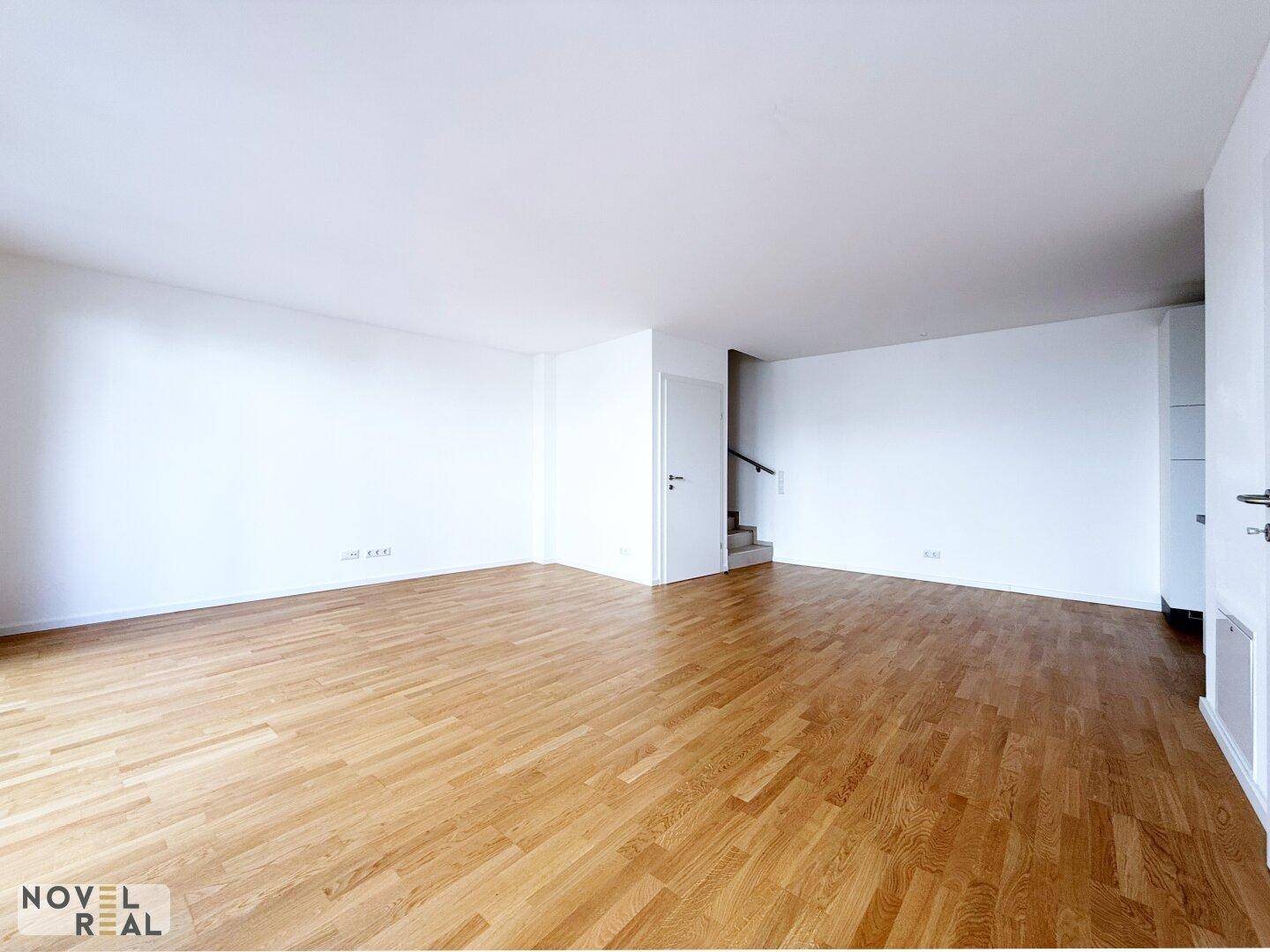 Großer, leerer Wohnbereich mit hellem Parkettboden und Zugang zu einer Treppe.