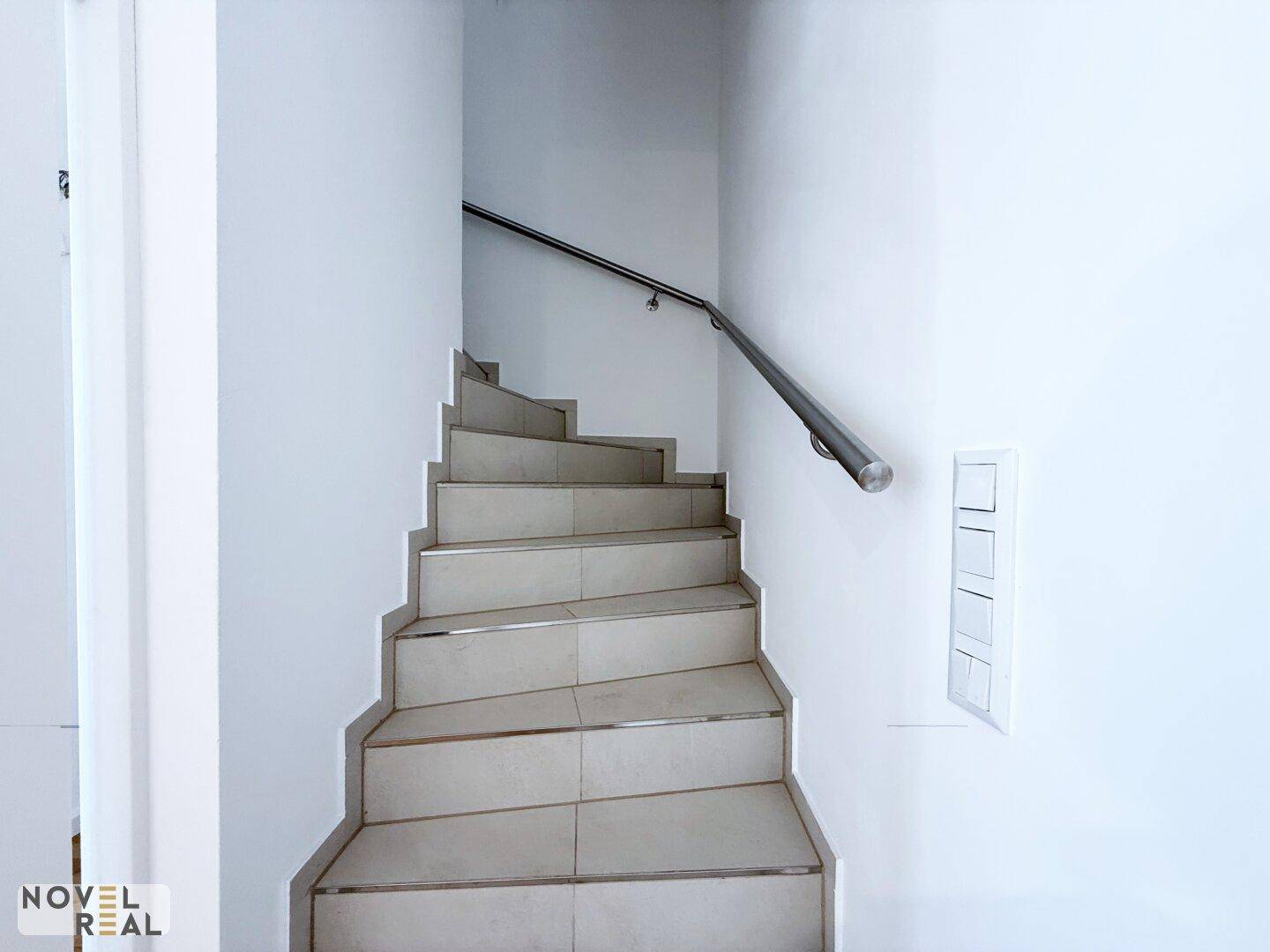 Moderne Treppe mit Fliesenstufen und Edelstahlgeländer, die in die oberen Etagen führt.