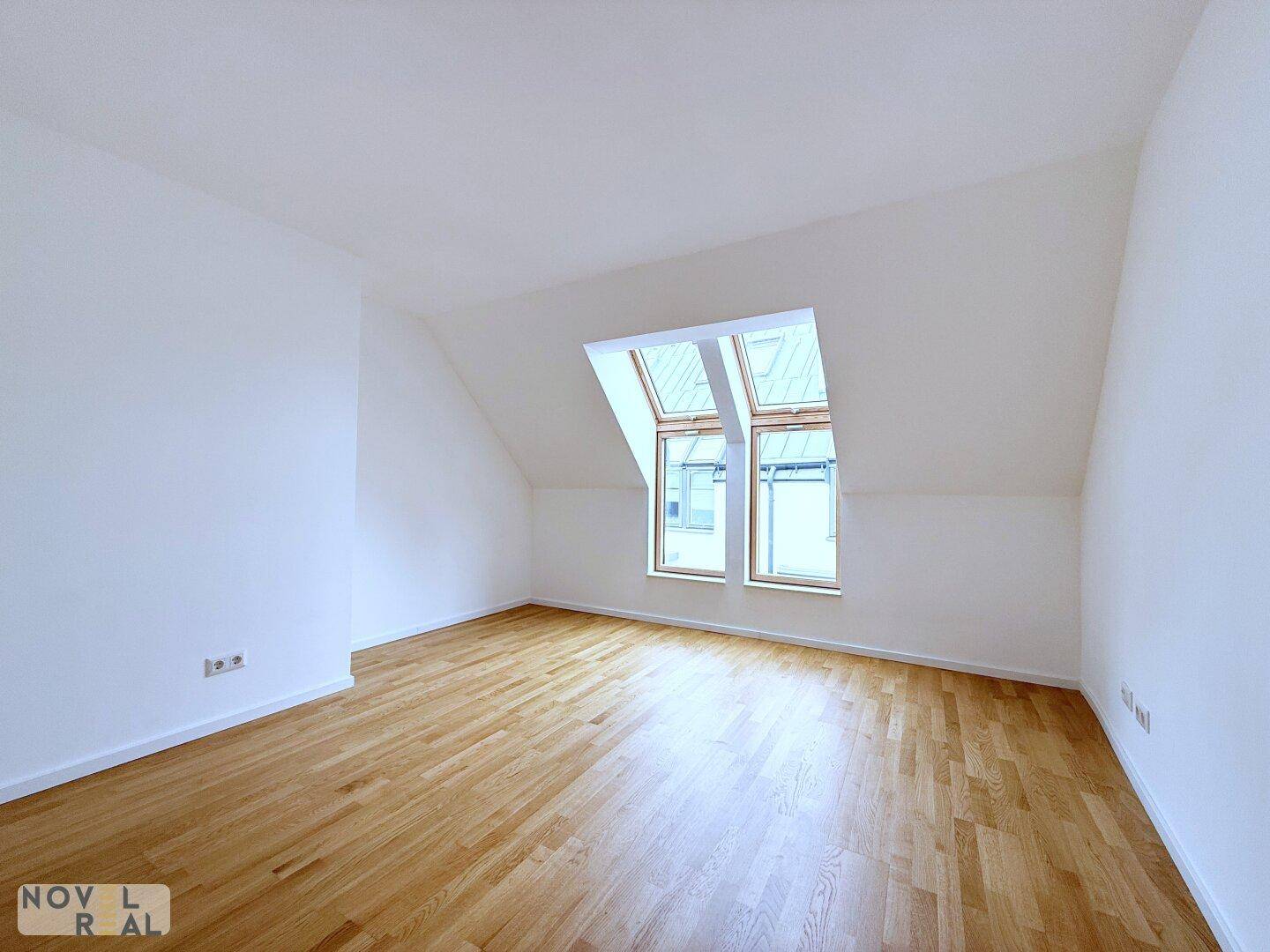 Helles Schlafzimmer im Dachgeschoss mit Parkettboden und schrägen Wänden sowie Dachfenstern.