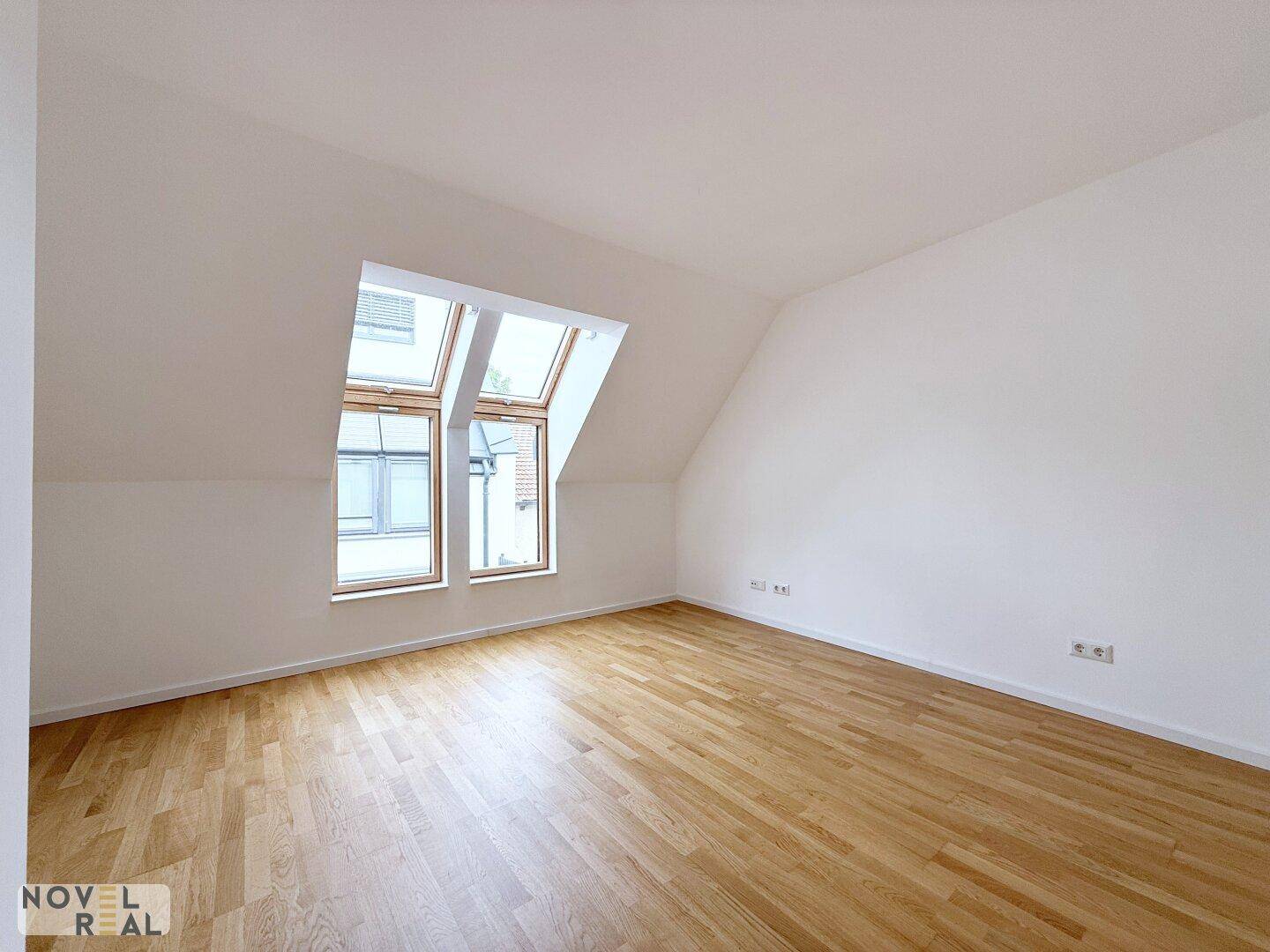 Geräumiges Dachzimmer mit Parkettboden und mehreren Dachfenstern, die viel Licht hereinlassen.