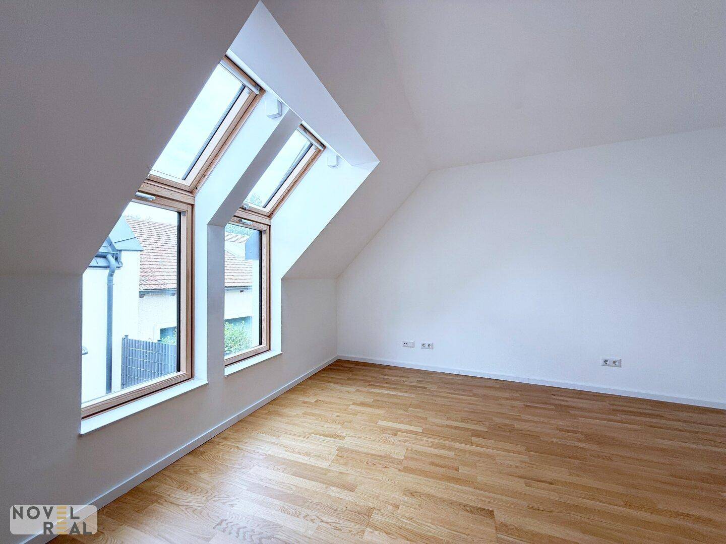 Dachgeschosszimmer mit Parkettboden und schrägen Wänden, ausgestattet mit großen Dachfenstern.