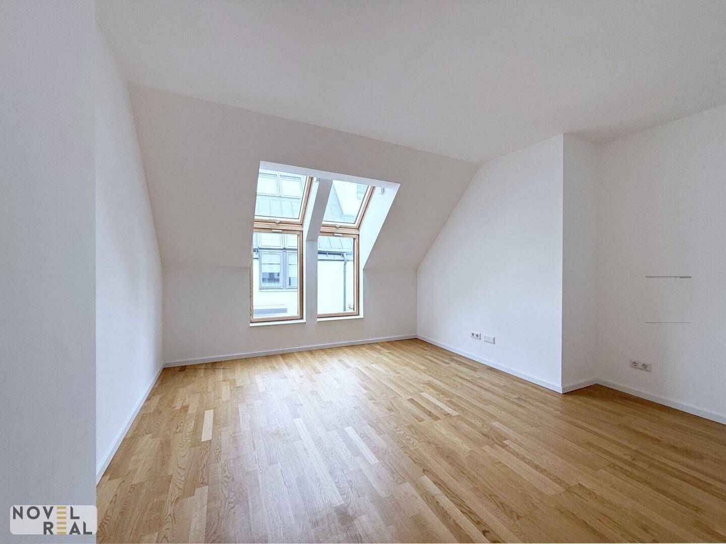 Dachgeschossraum mit Parkettboden und schrägen Wänden, der durch die Dachfenster gut belichtet ist.