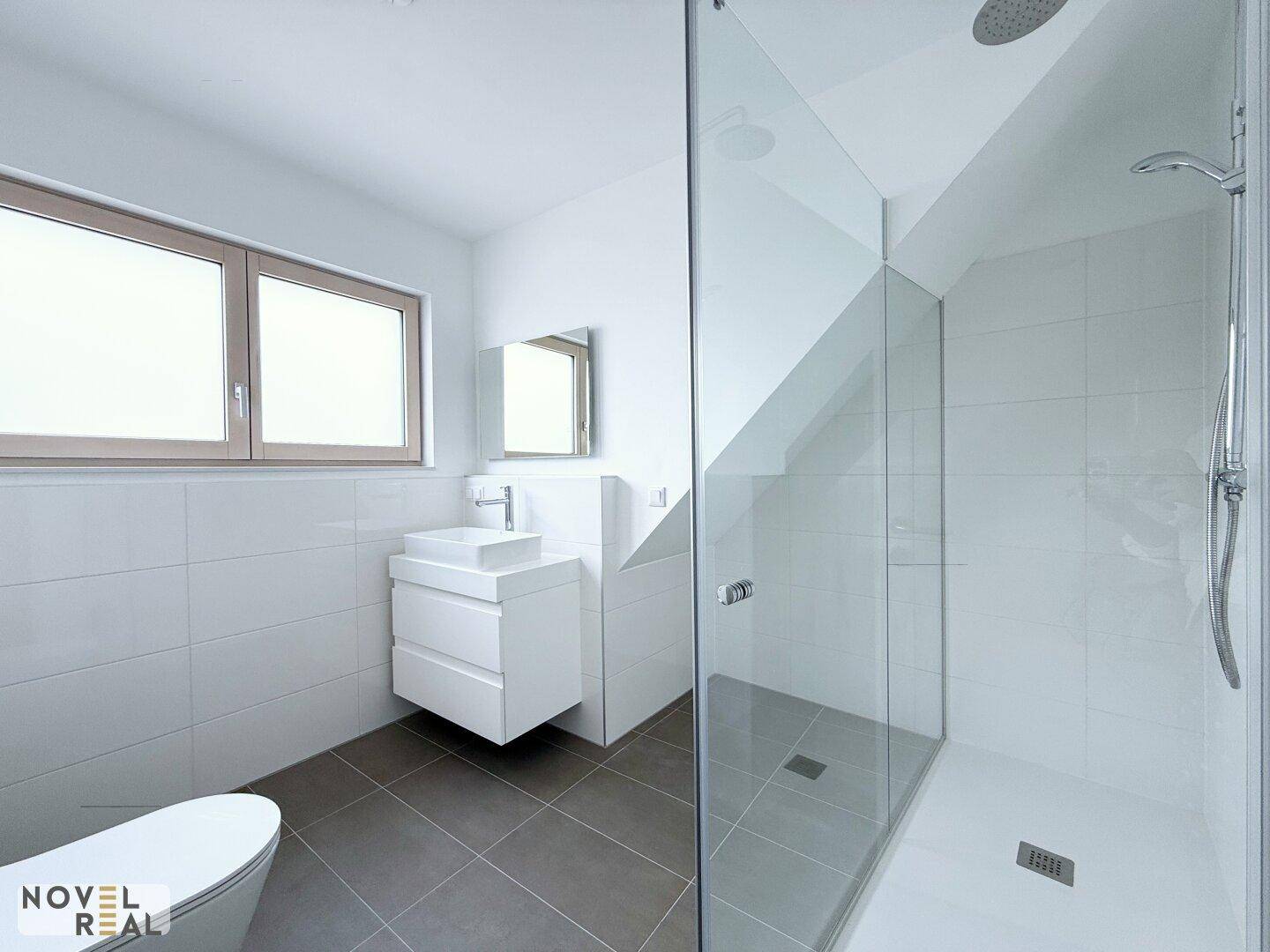 Modernes Badezimmer mit ebenerdiger Dusche, Hänge-WC und Fenster für natürliche Belüftung.