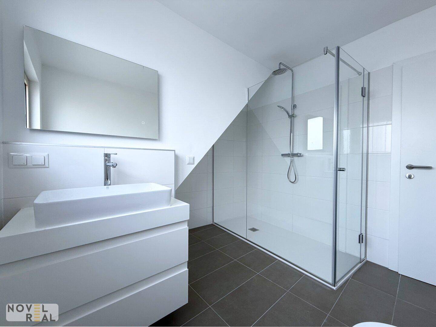 Zeitgemäßes Badezimmer mit großer Glasdusche, modernem Waschtisch und großem Spiegel.