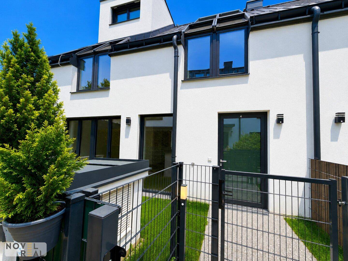 Rückseite eines modernen Reihenhauses mit großen Fenstern und Zugang zum privaten Gartenbereich.